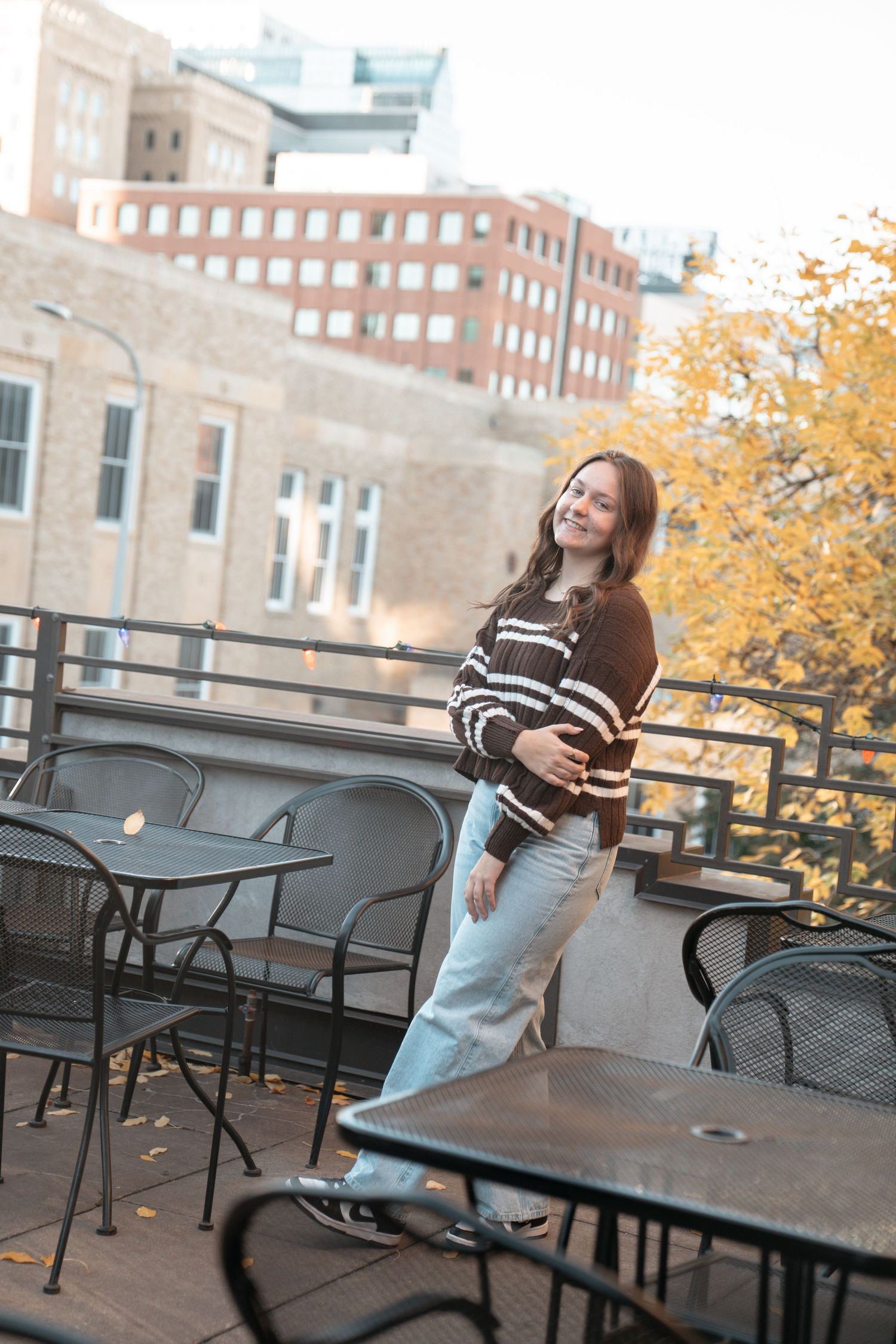 Autumn scene on a rooftop patio with metal furniture and fall foliage in the background.
