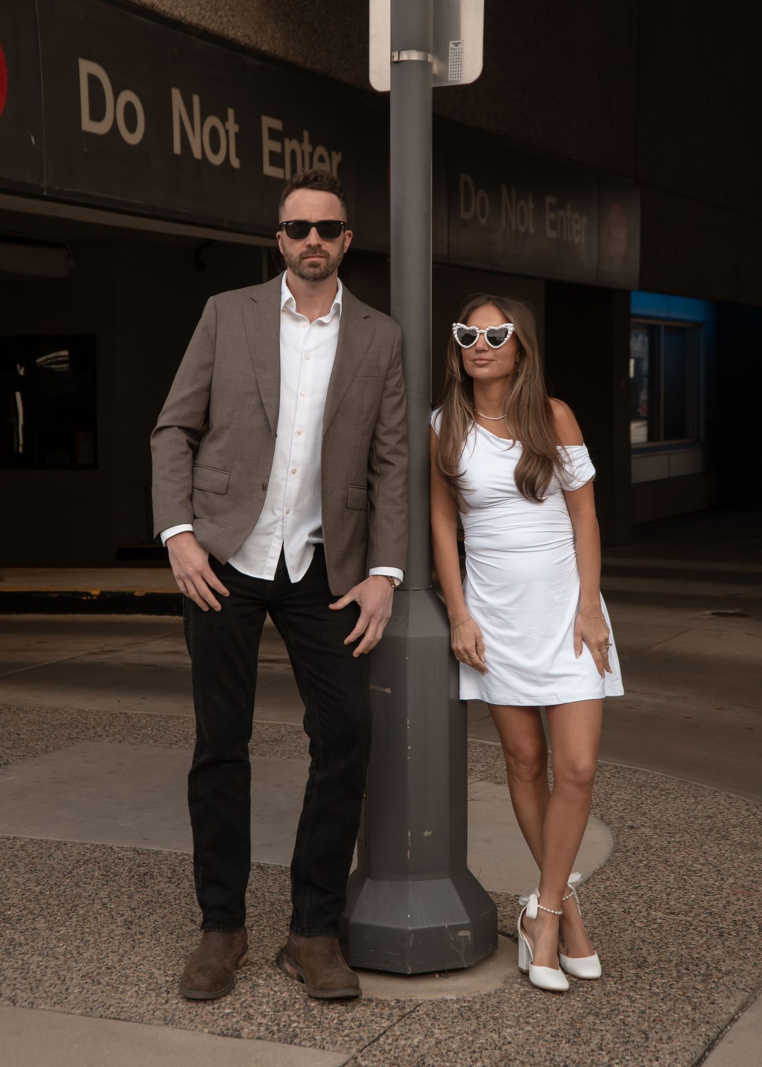 Stylish couple poses near a 'Do Not Enter' sign in an urban setting.