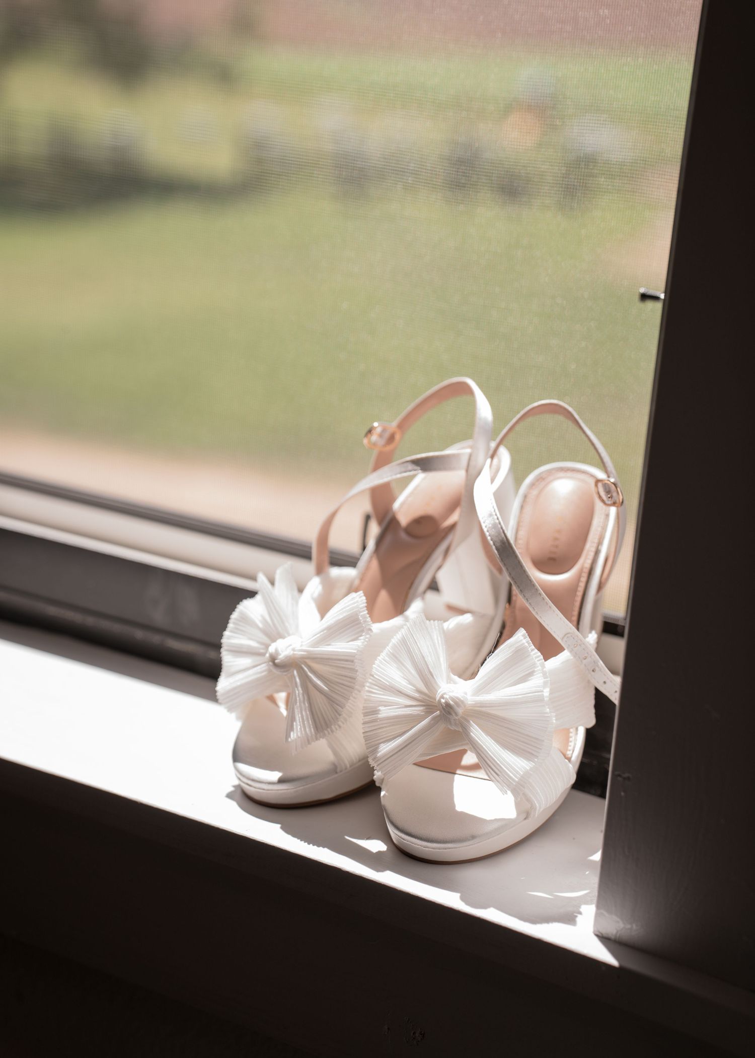 Elegant white wedding shoes displayed on a sunny windowsill.