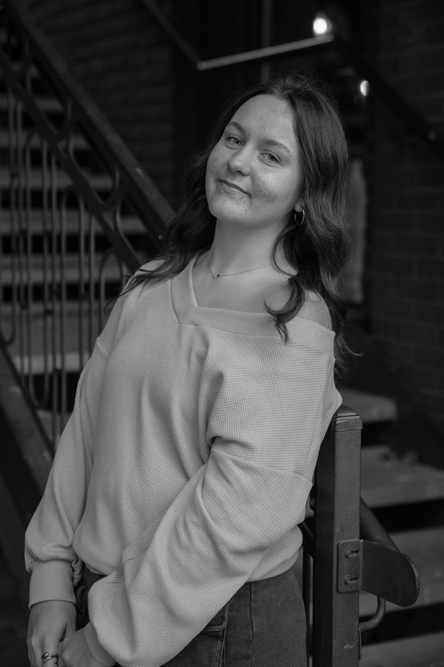 Monochrome portrait showing a relaxed pose against metal railings in low light.