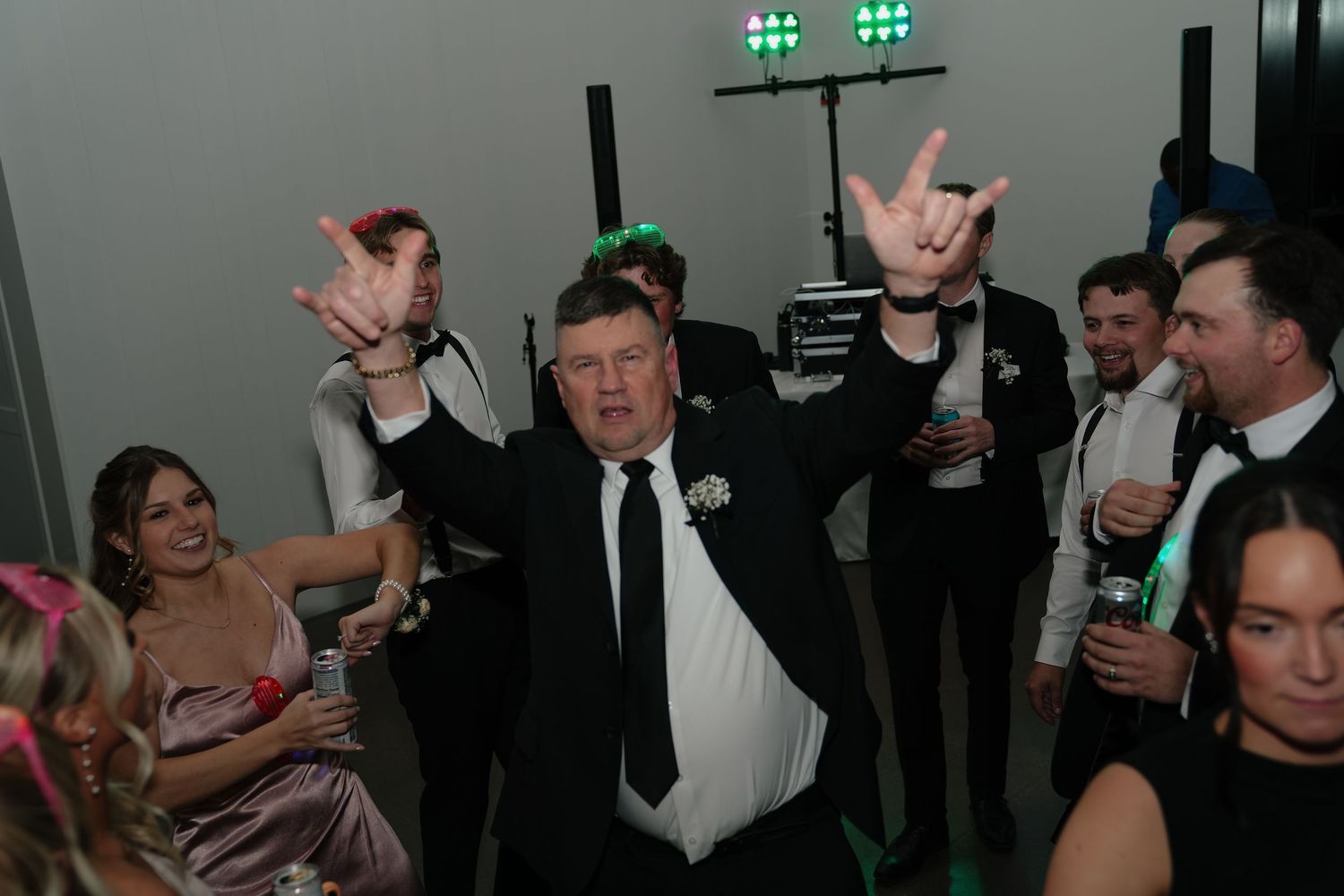 Guests celebrating at a wedding reception, dancing and making rock on hand gestures in formal attire.