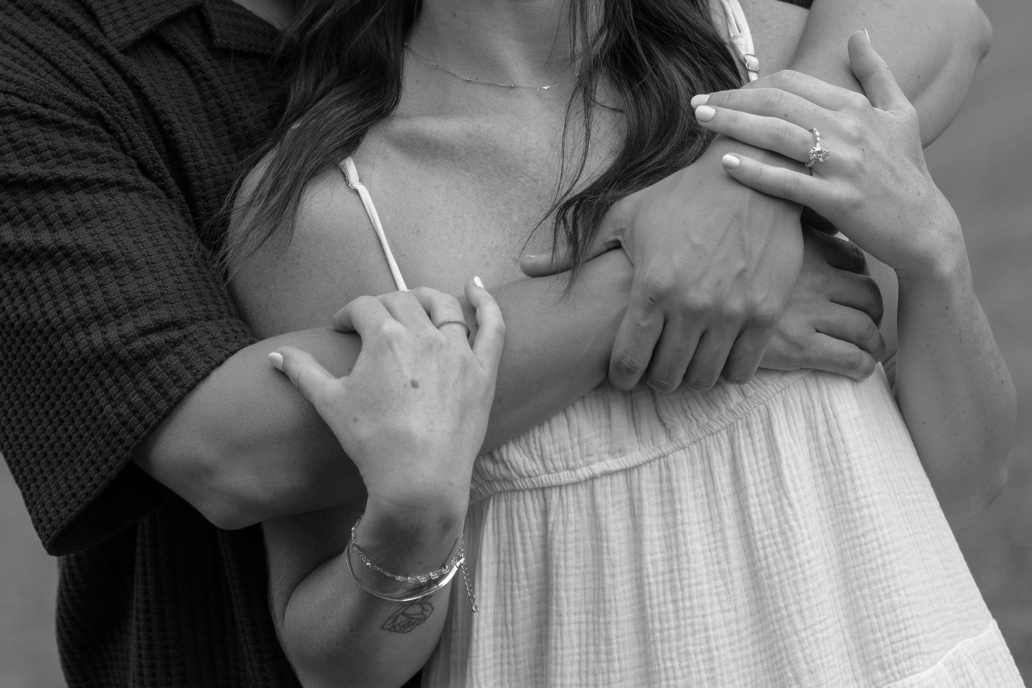 Black and white photo of a couple embracing, woman in white dress with bracelet, man holding her gently.