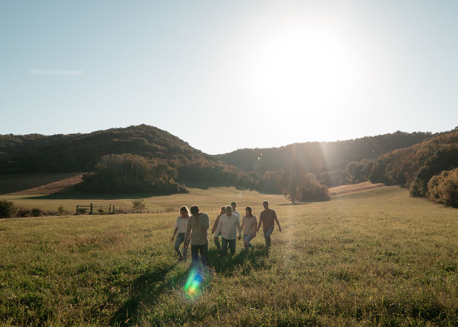 Scenic sunset landscape with silhouettes of people walking across a hilltop meadow.