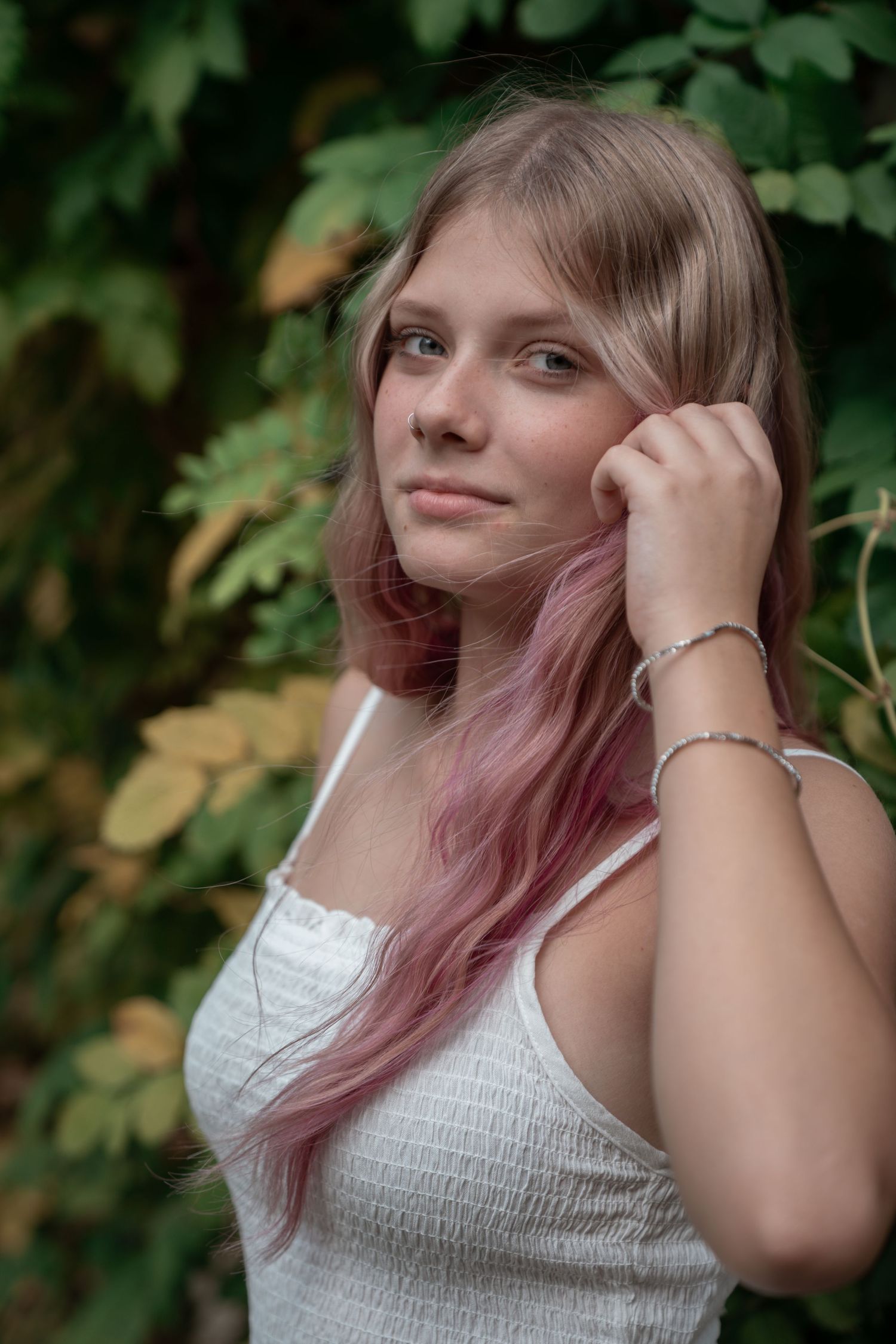 Portrait in a garden setting featuring white summer top and pink-tinted hair against lush foliage.