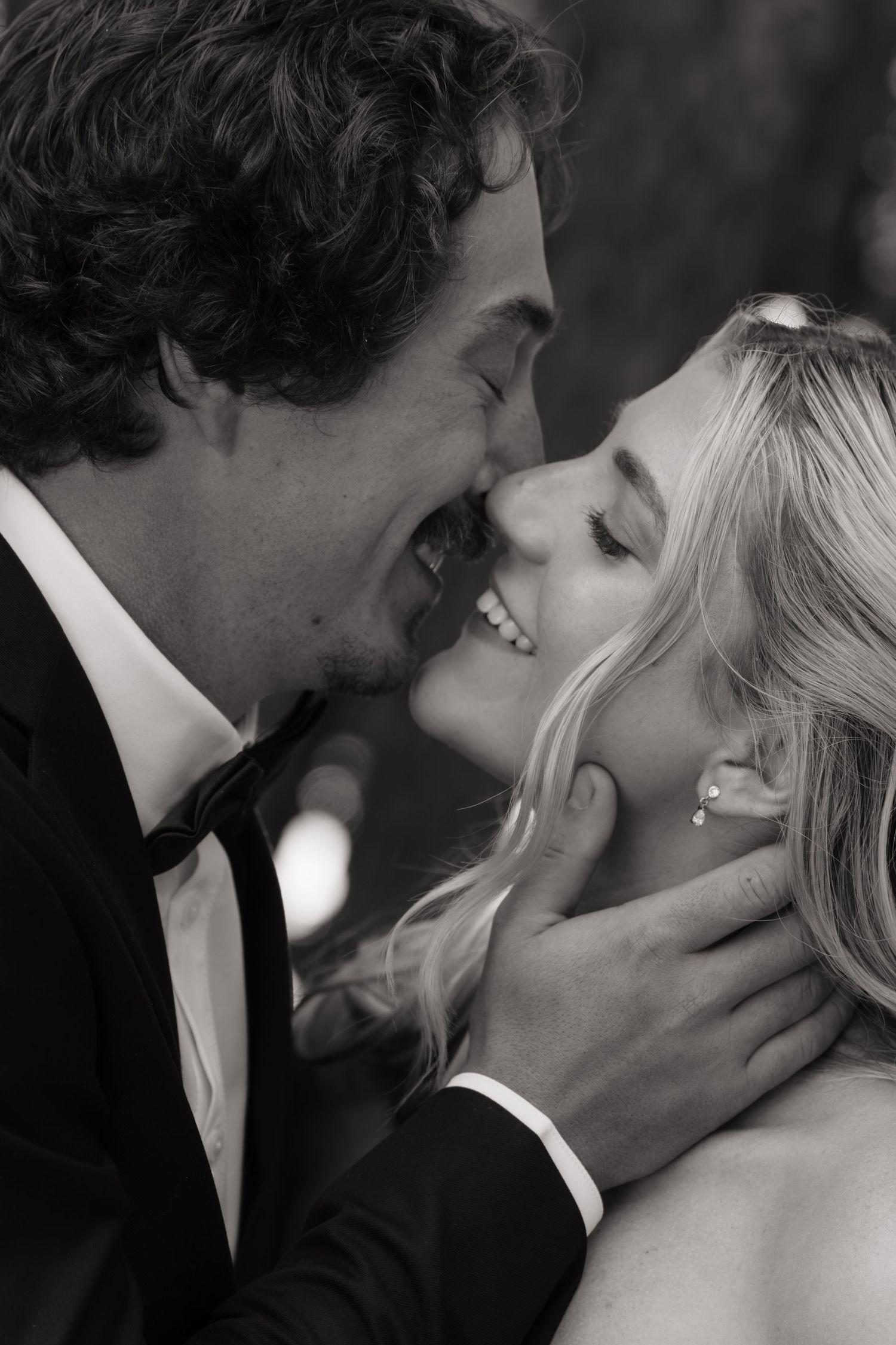 Black and white photo of a smiling bride and groom sharing a romantic moment, groom gently holding bride's face.