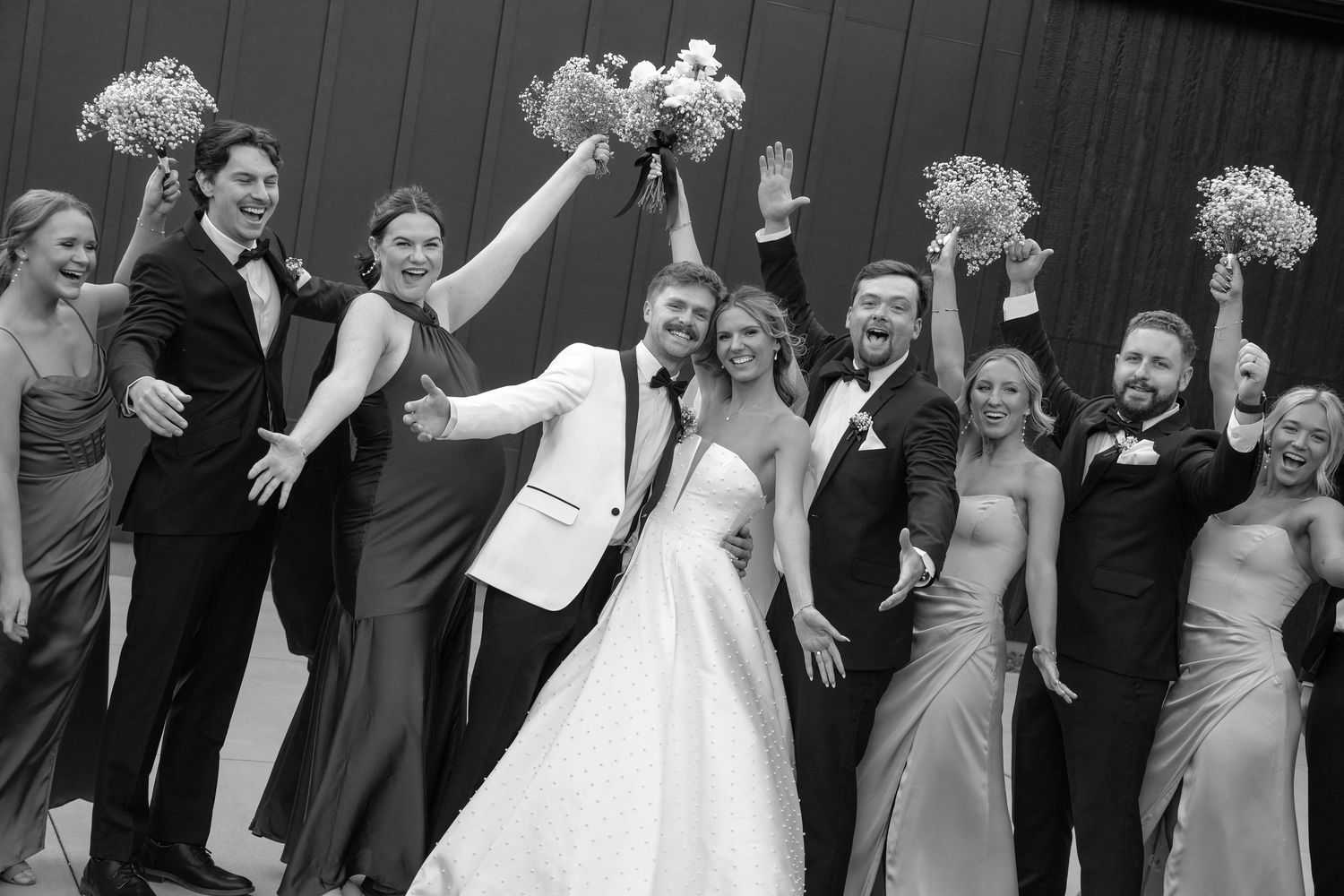 Wedding party celebrates with arms raised in joy during outdoor black and white photo sequence. White and Sable wedding venue, Ham Lake, MN.