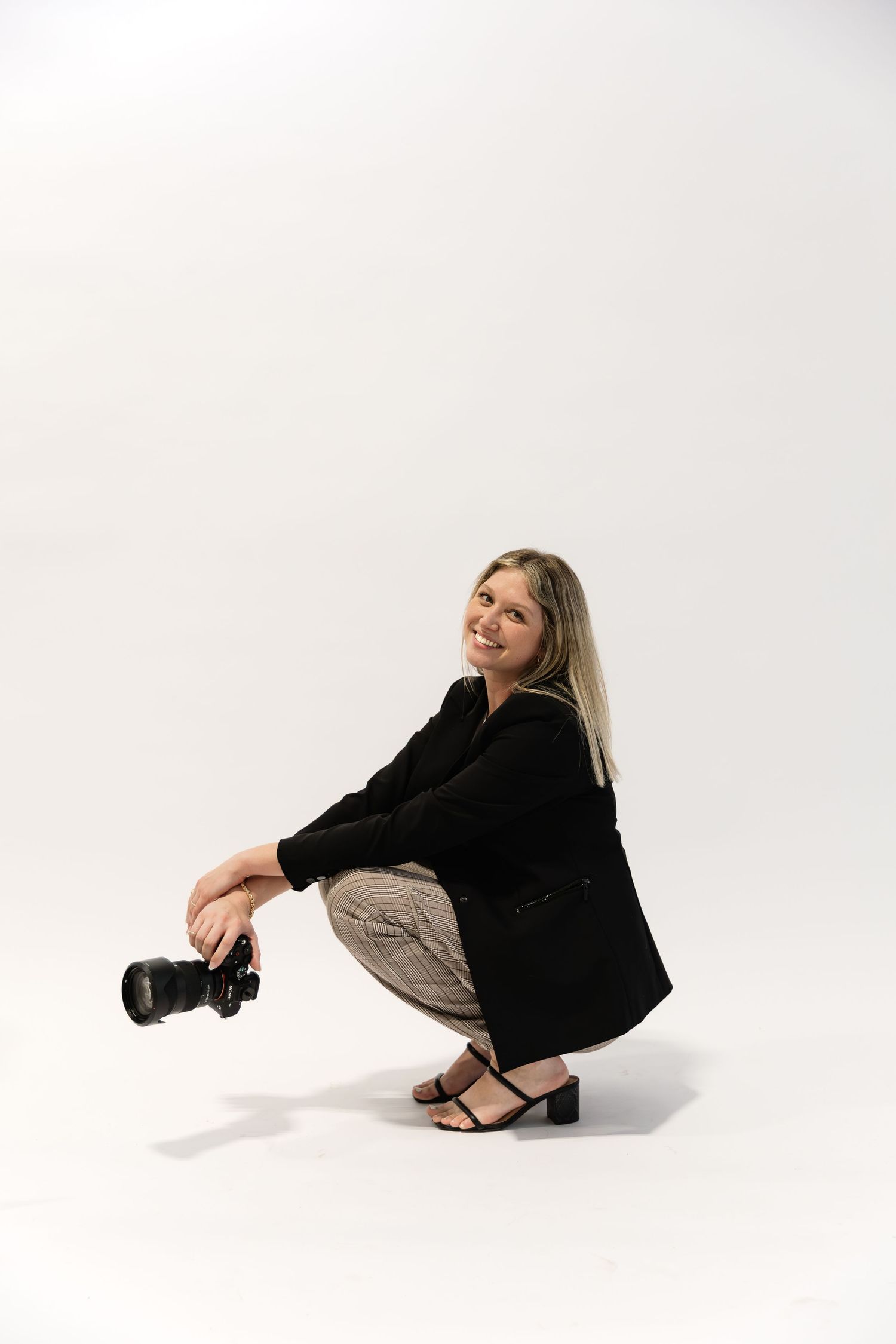 A series of four fashion poses showing someone in a black sweater and beige pants sitting on a white studio floor.