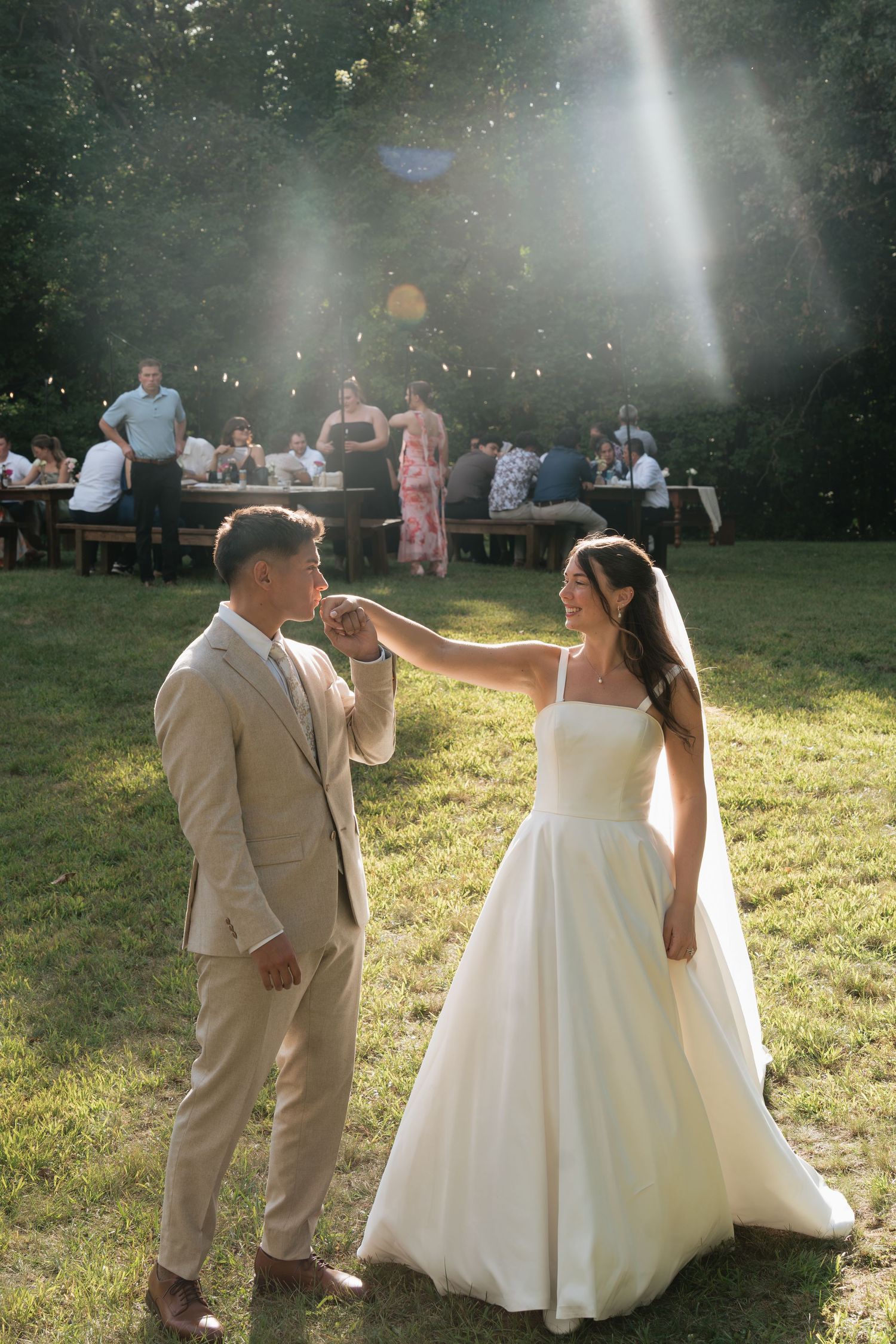 Bride and groom share first dance outdoors at golden hour wedding reception with guests seated at long tables in background.