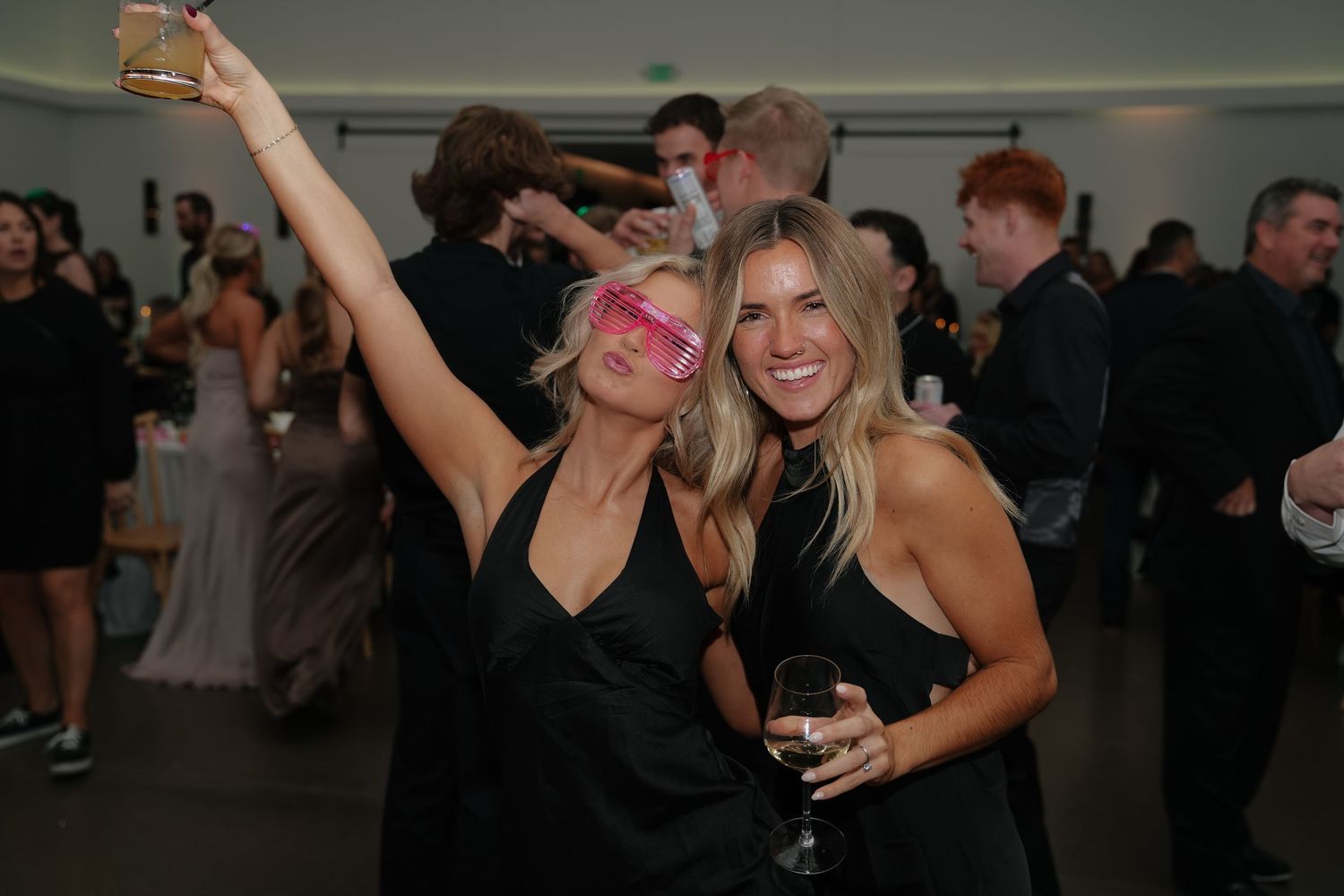 People dancing and celebrating at a wedding reception with raised arms on a crowded dance floor.