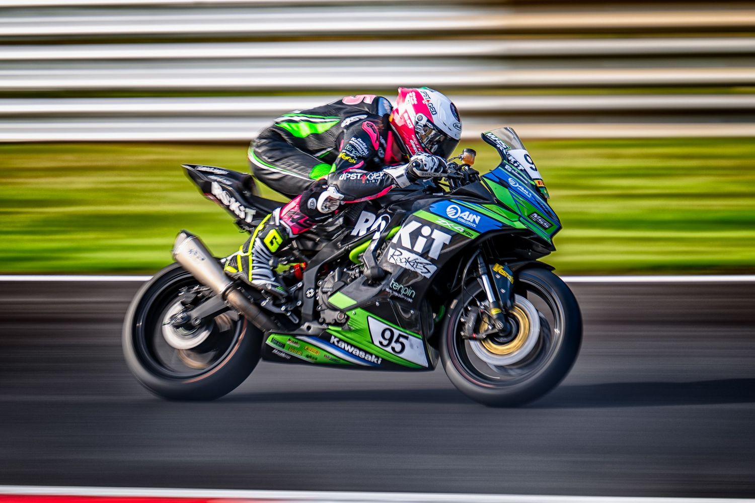 A motorcycle racer leans into a turn at high speed on a green Kawasaki racing bike with motion blur effect.