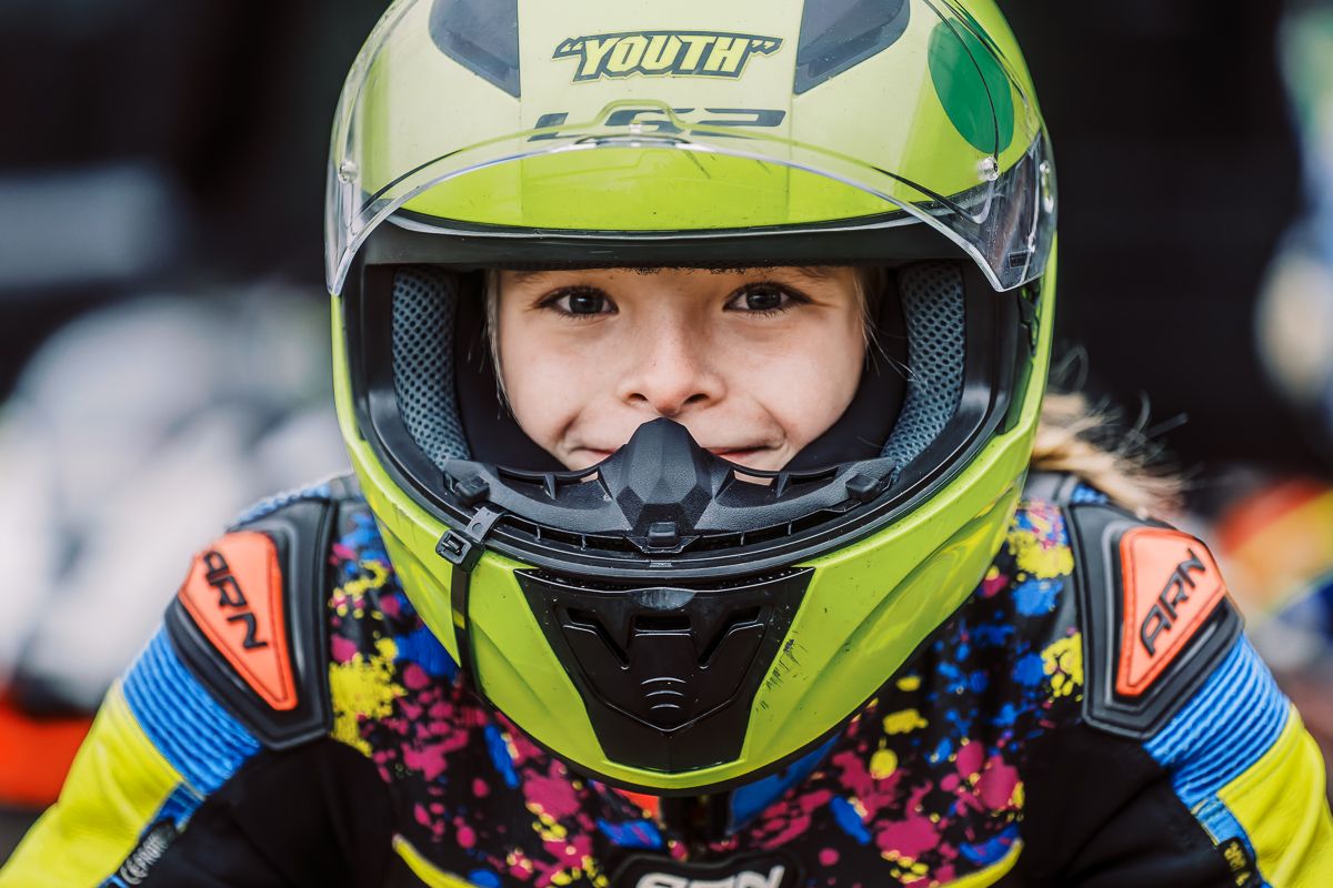 Racing motorcycles line up on track wearing colorful protective gear and helmets.