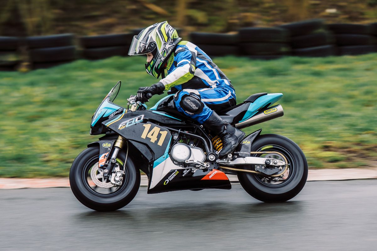 Motorcycle racer leans into a turn on a turquoise sportbike during high-speed racing competition.