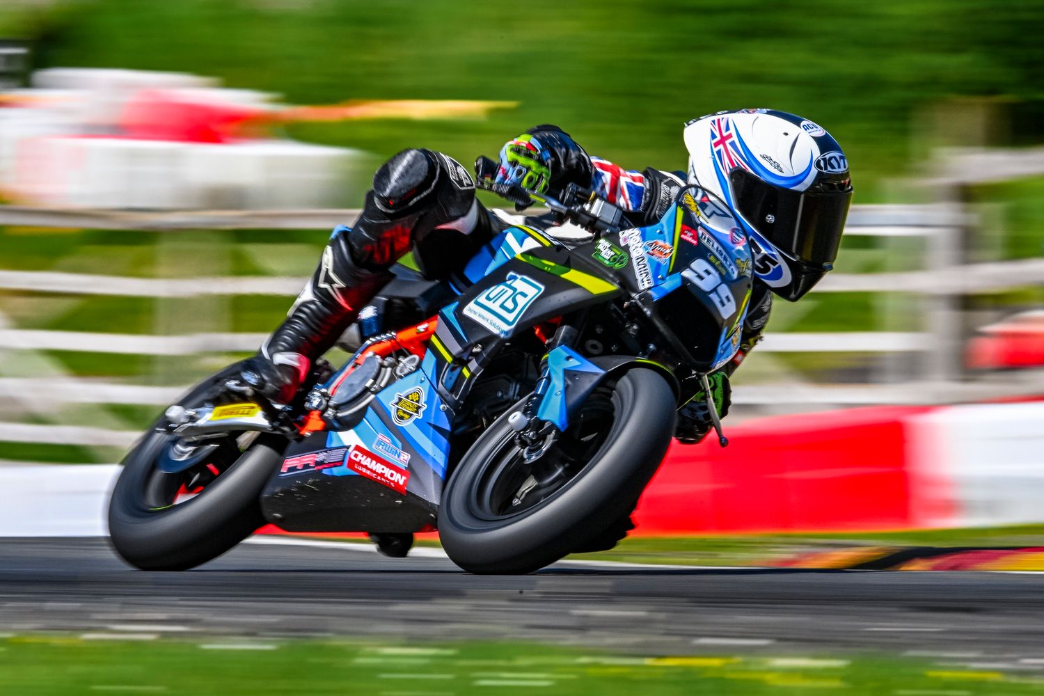 A motorcycle racer leans into a turn on a sport bike during a professional road race on a lush green circuit.