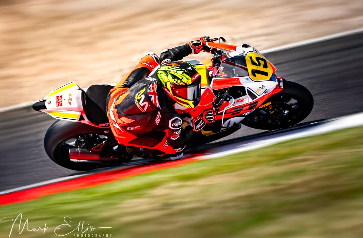 A motorcycle racer leans into a turn at high speed on a racing circuit, captured with motion blur effect.