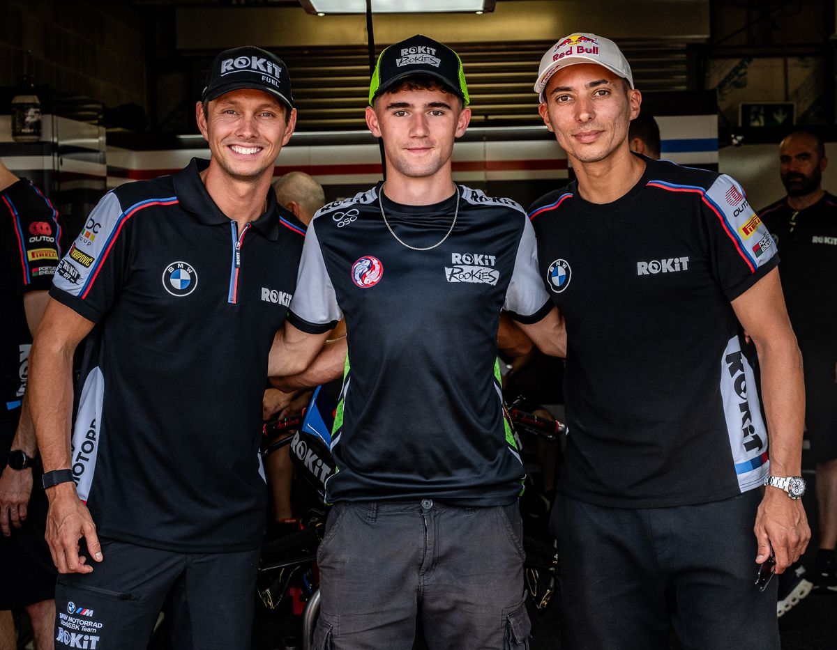 Racing team members wearing black BMW Motorrad uniforms pose together at a motorsport event.