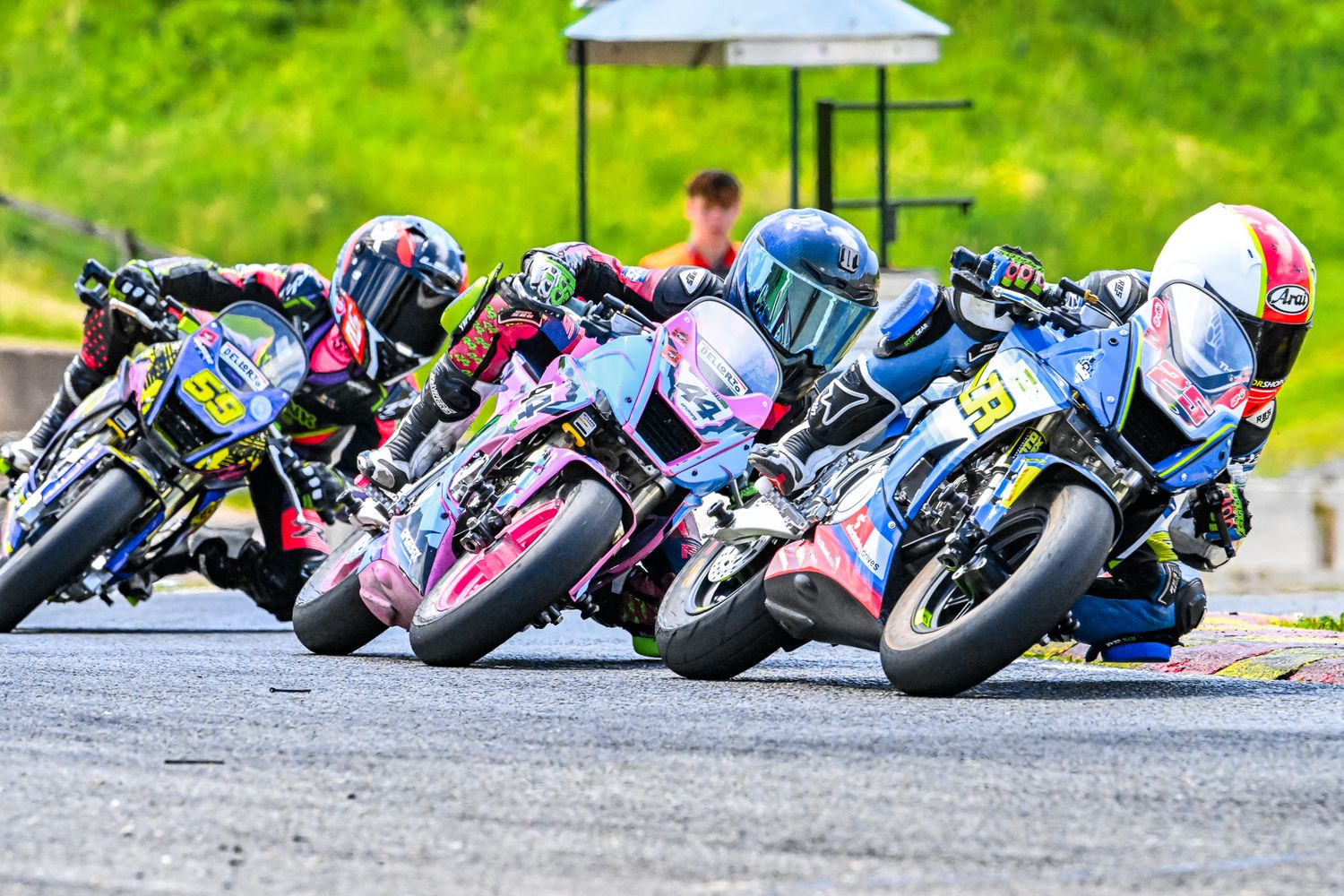 Motorcycle racers leaning into a sharp turn during a competitive track race on a sunny day.