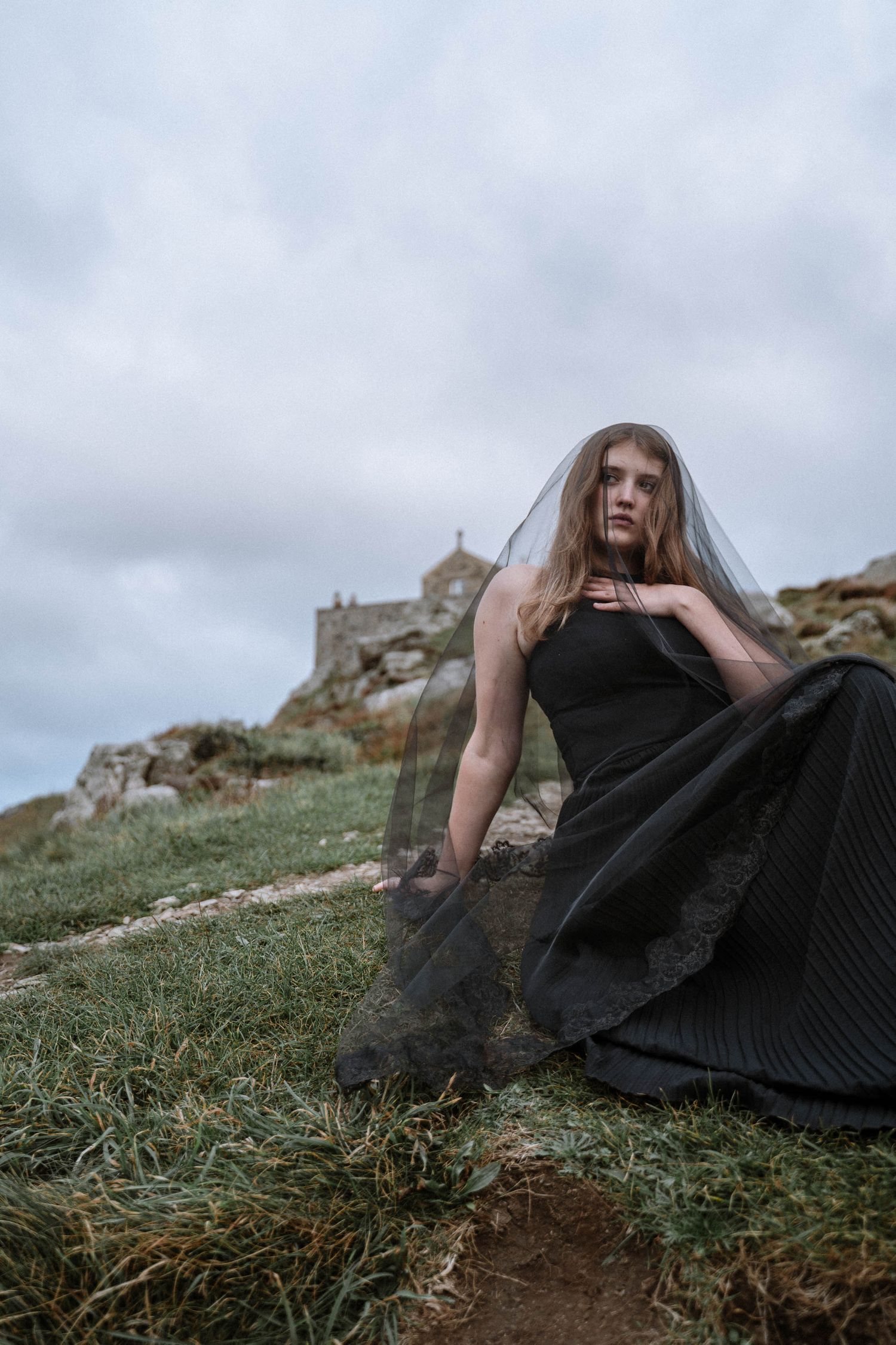 Person in black dress with veil near St Nicholas Chapel during a St Ives elopement with gothic styling and cliffs