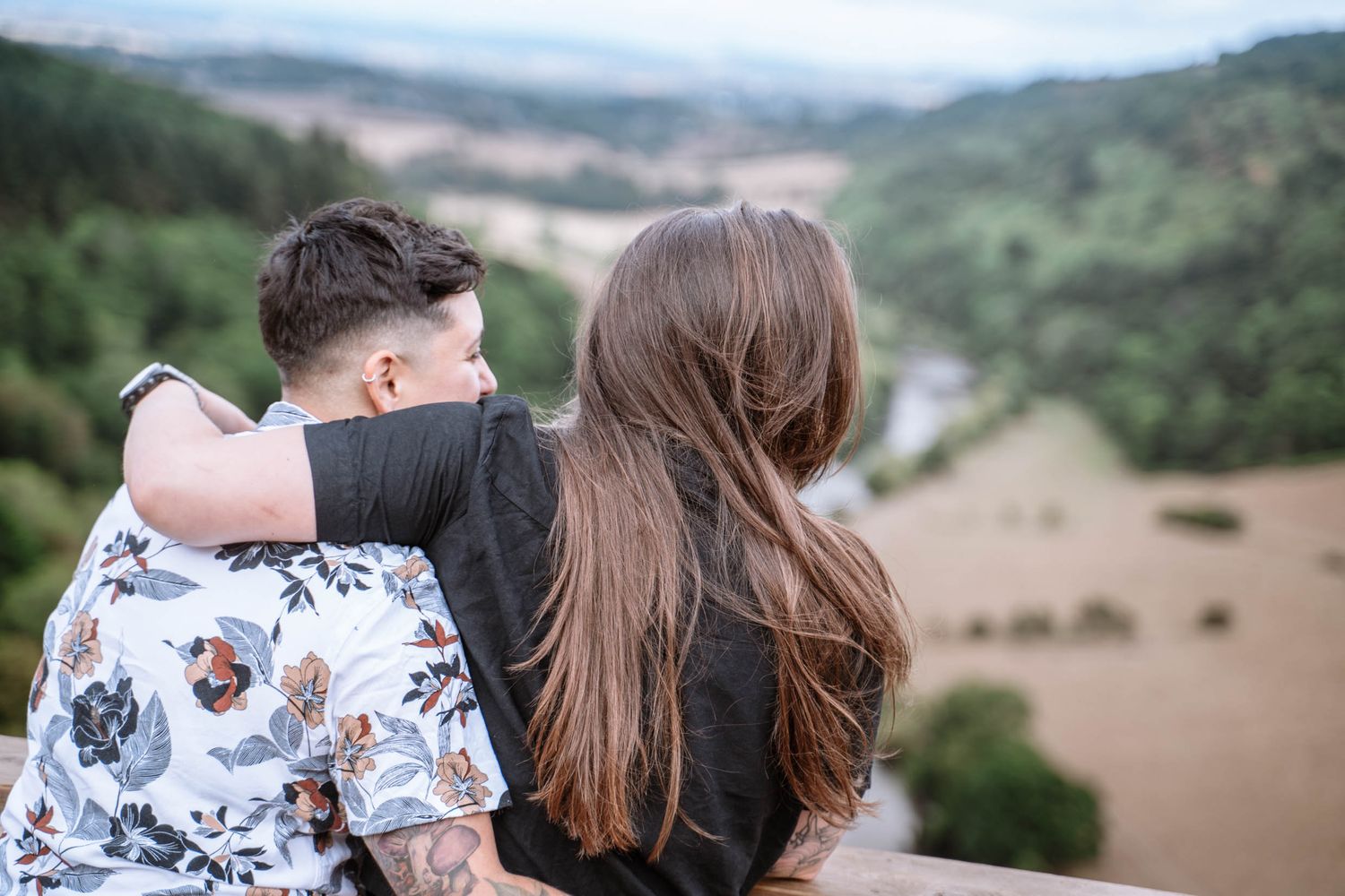 A queer couple stand arm in arm overlooking the River Wye and surrounding valley.