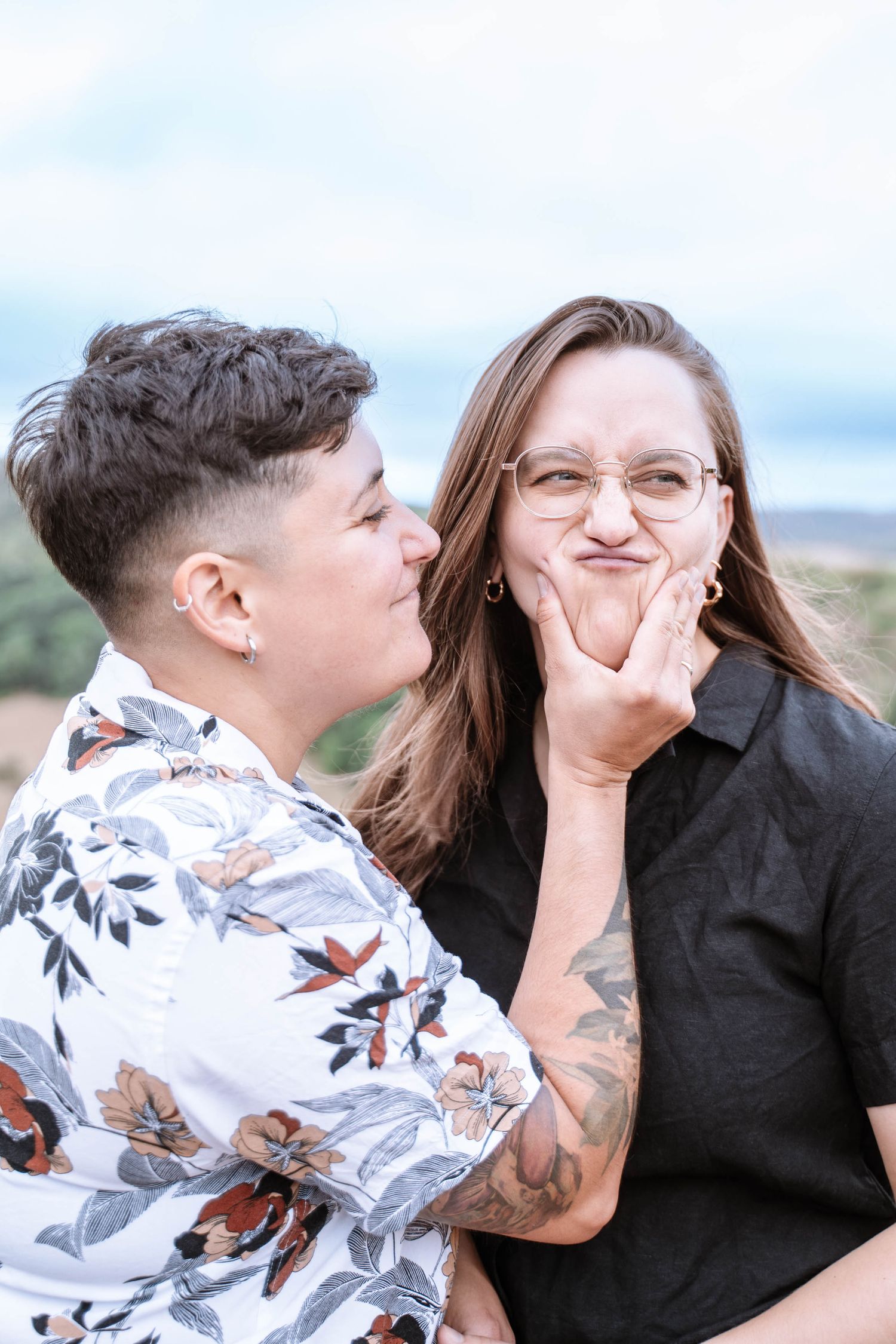 A lesbian couple smile as one gently touches the other’s cheek.