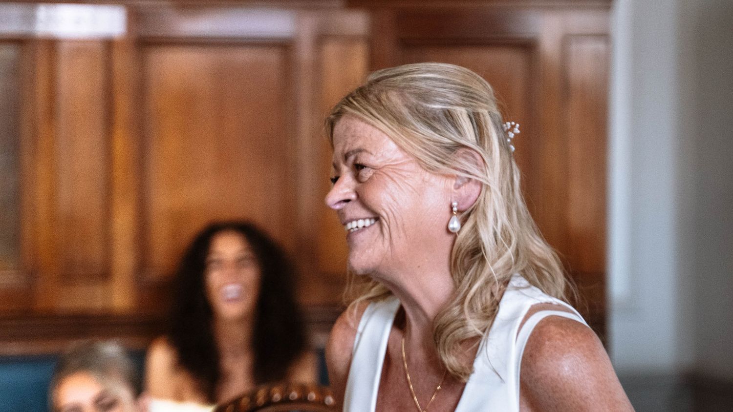 Woman smiling during the wedding ceremony inside Waterloo Town Hall's Council Chamber, guests seated behind her