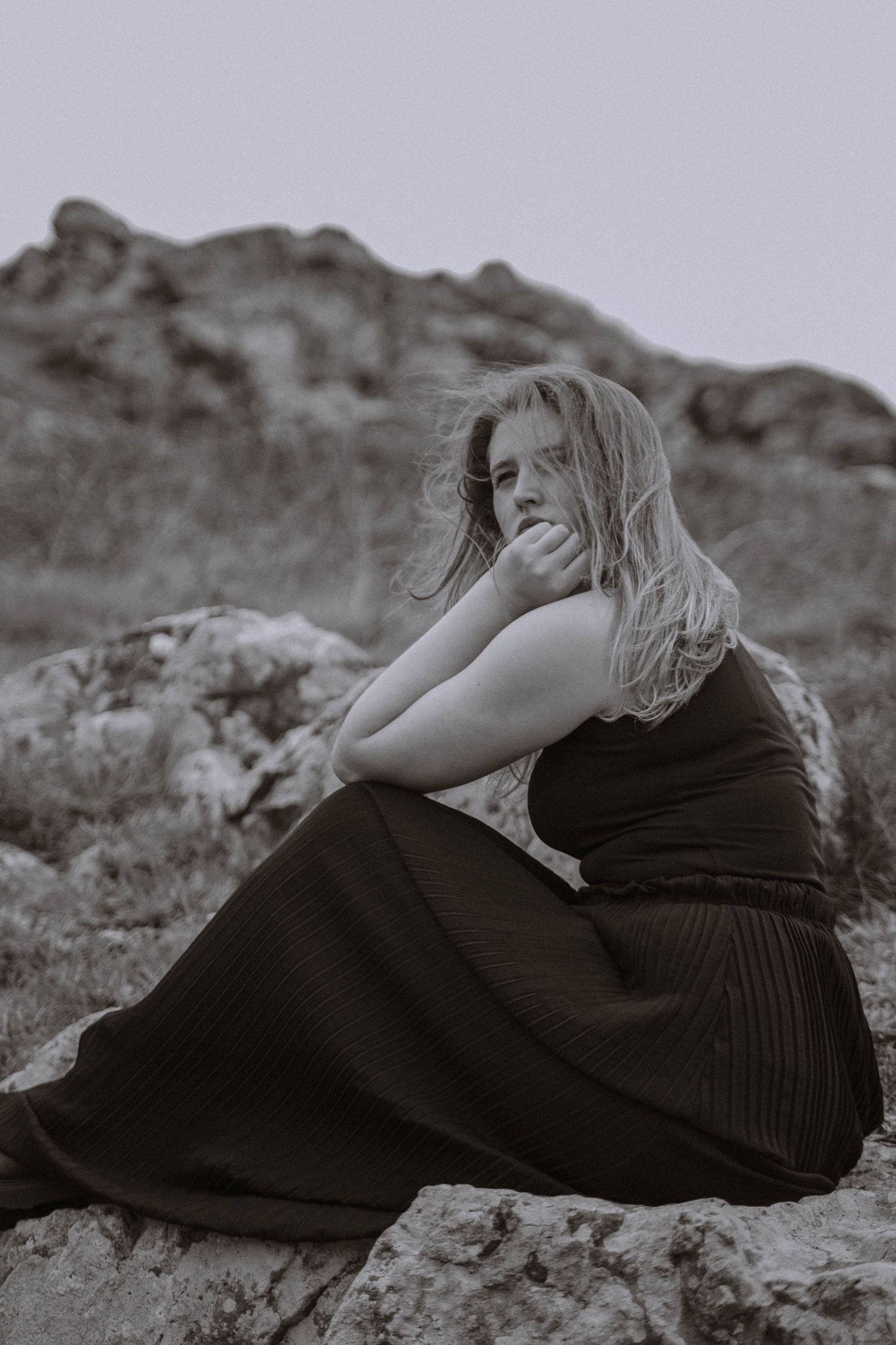 Black and white seated portrait on rocks with windswept hair during a Gothic St Ives Cornwall elopement scene