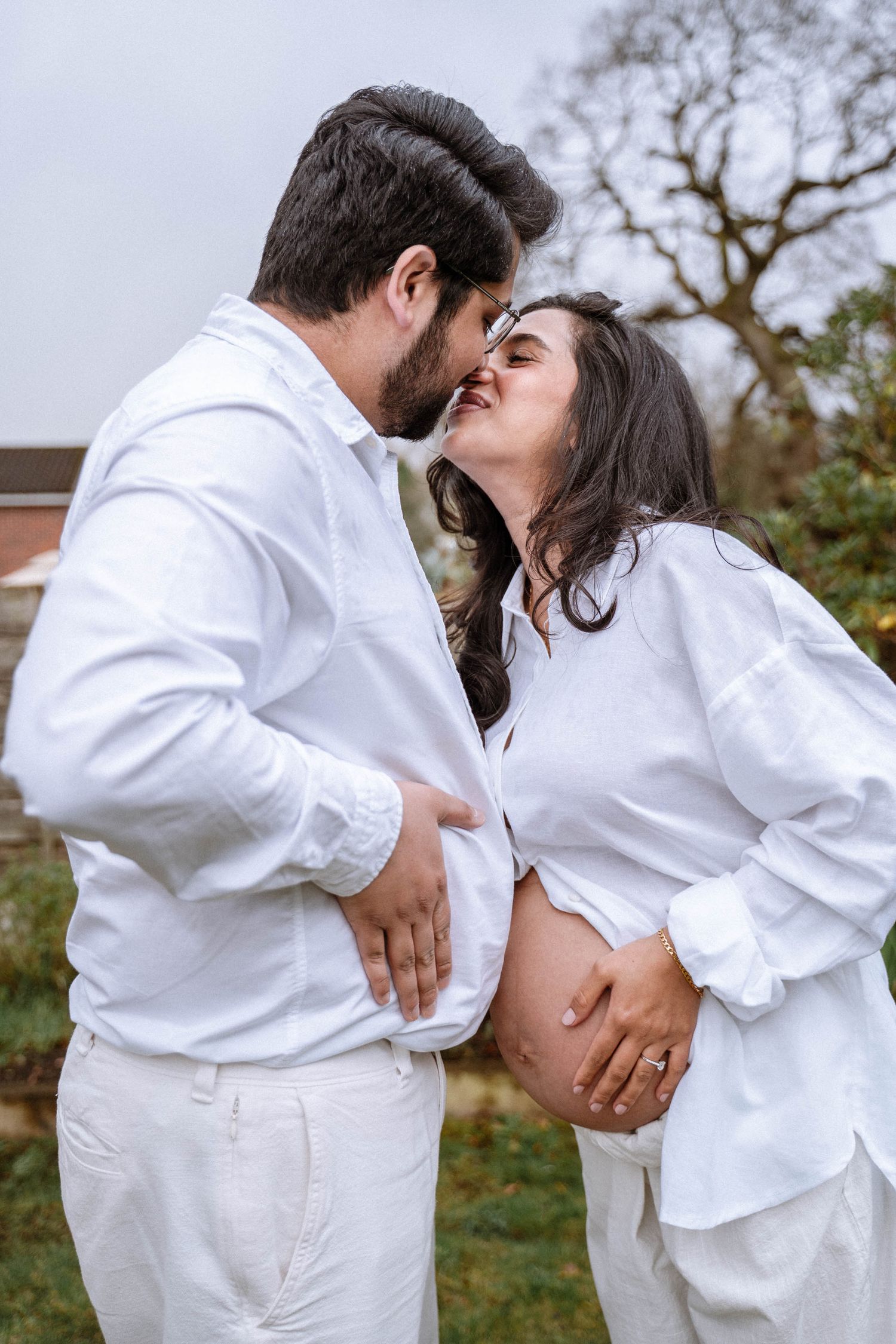 Maimoona and her partner kissing outdoors with their hands resting on her baby bump during a Manchester maternity shoot