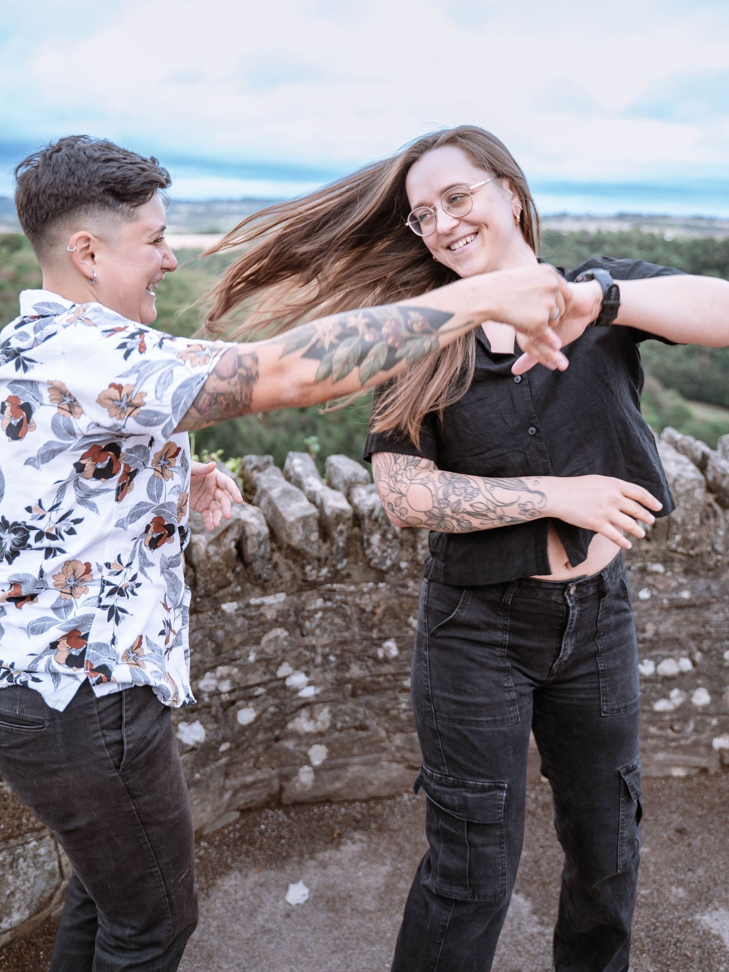A newly engaged queer couple spin one another beside the stone wall at Yat Viewpoint.