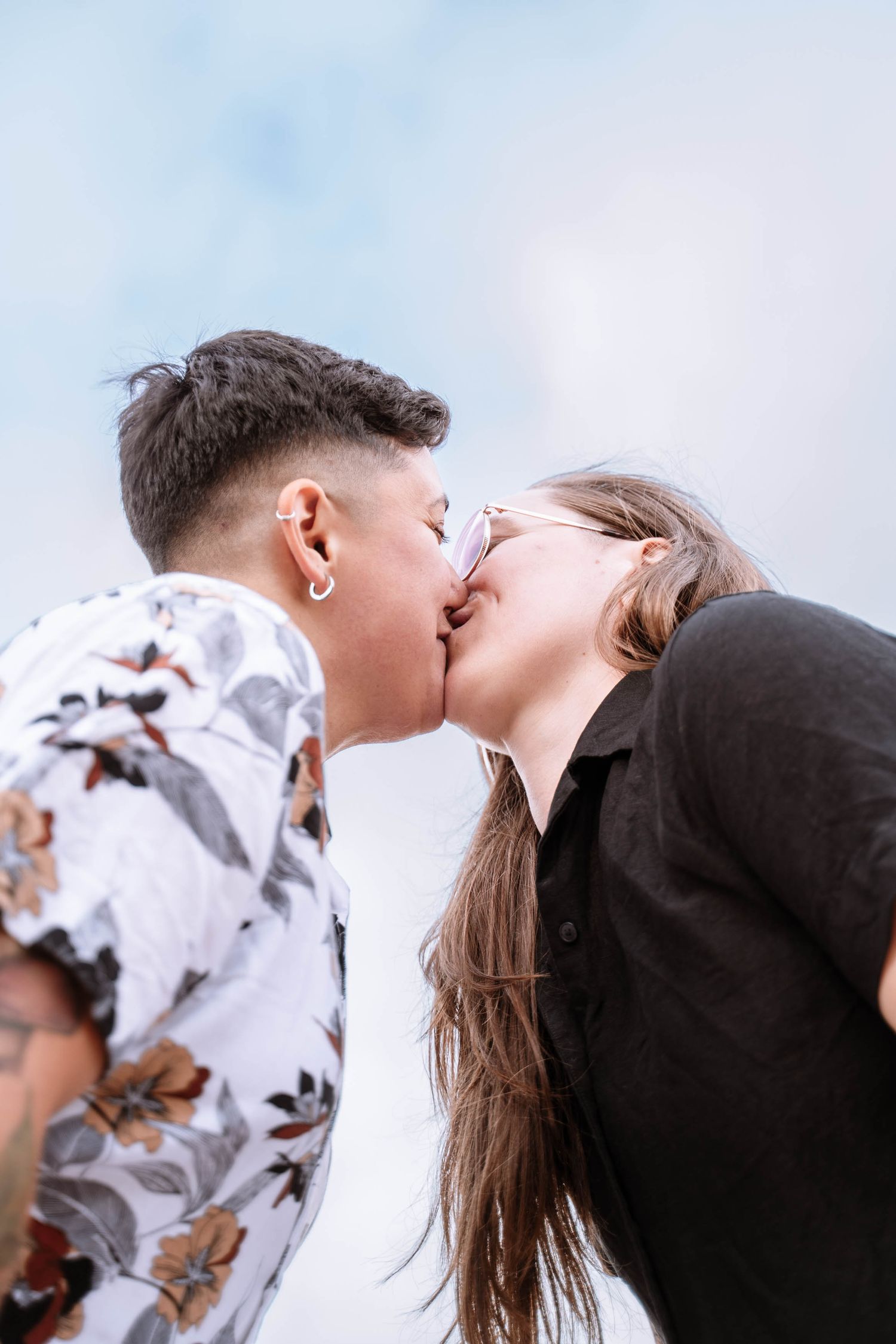 A queer couple kiss beneath the cloudy sky at Symonds Yat Rock.