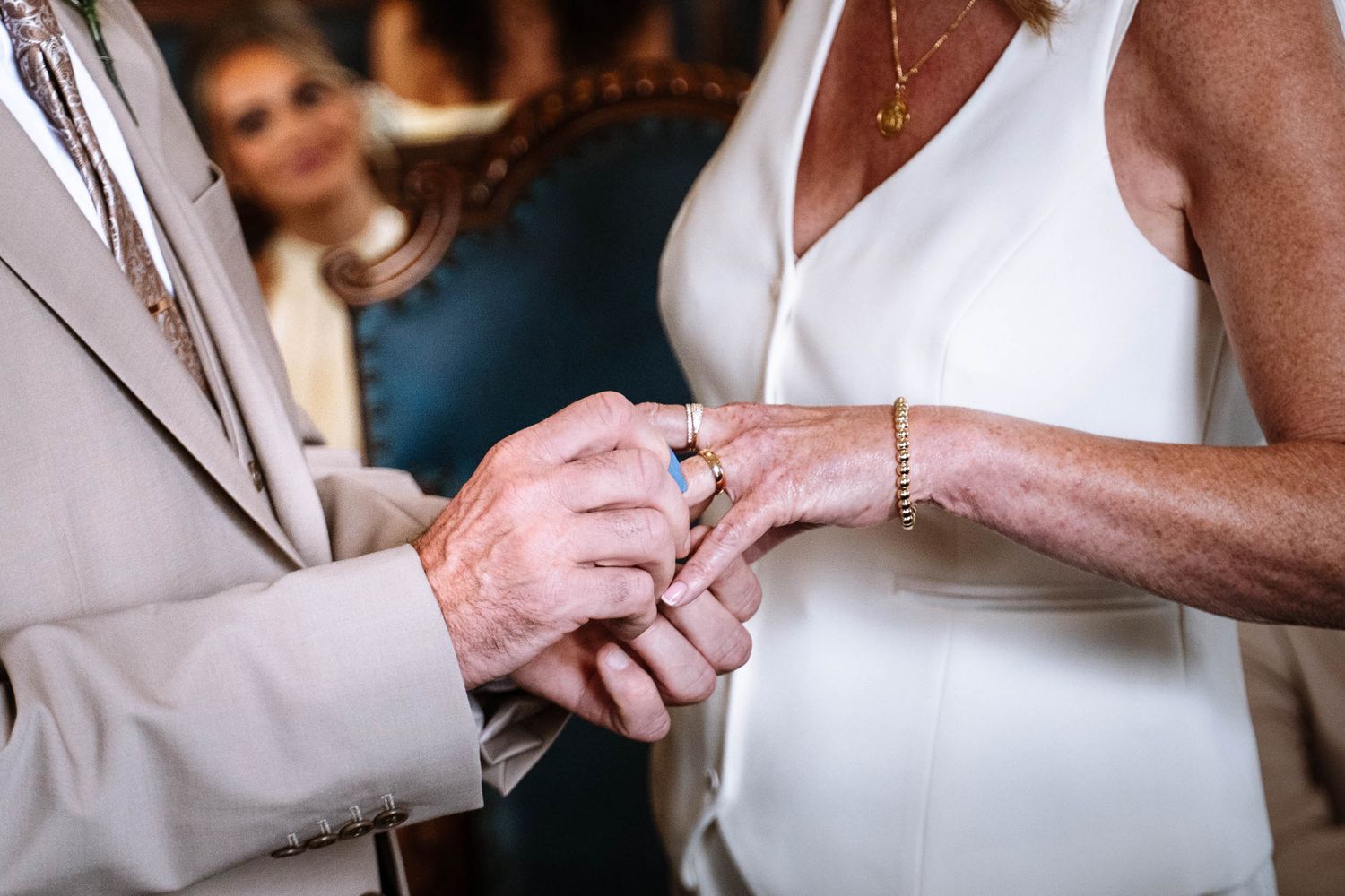 Close-up of a ring being placed on a hand during the ceremony at Waterloo Town Hall, with a guest seated in the background