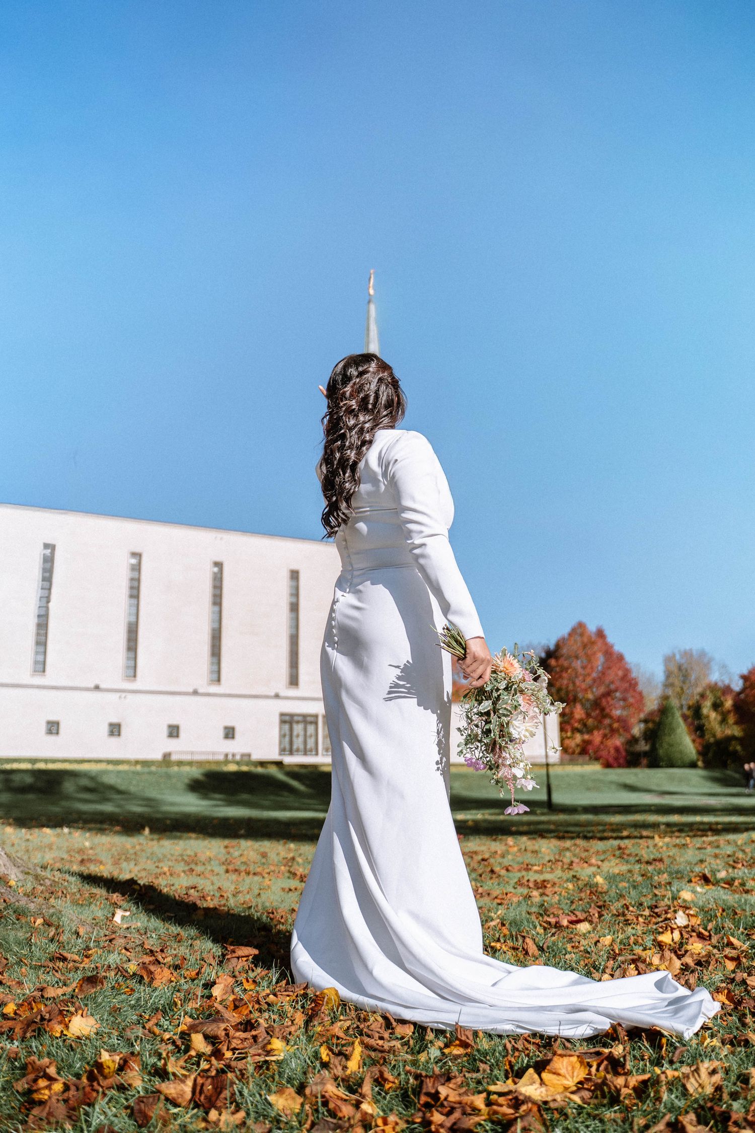 Bride standing outdoors in wedding dress near LDS temple during autumn