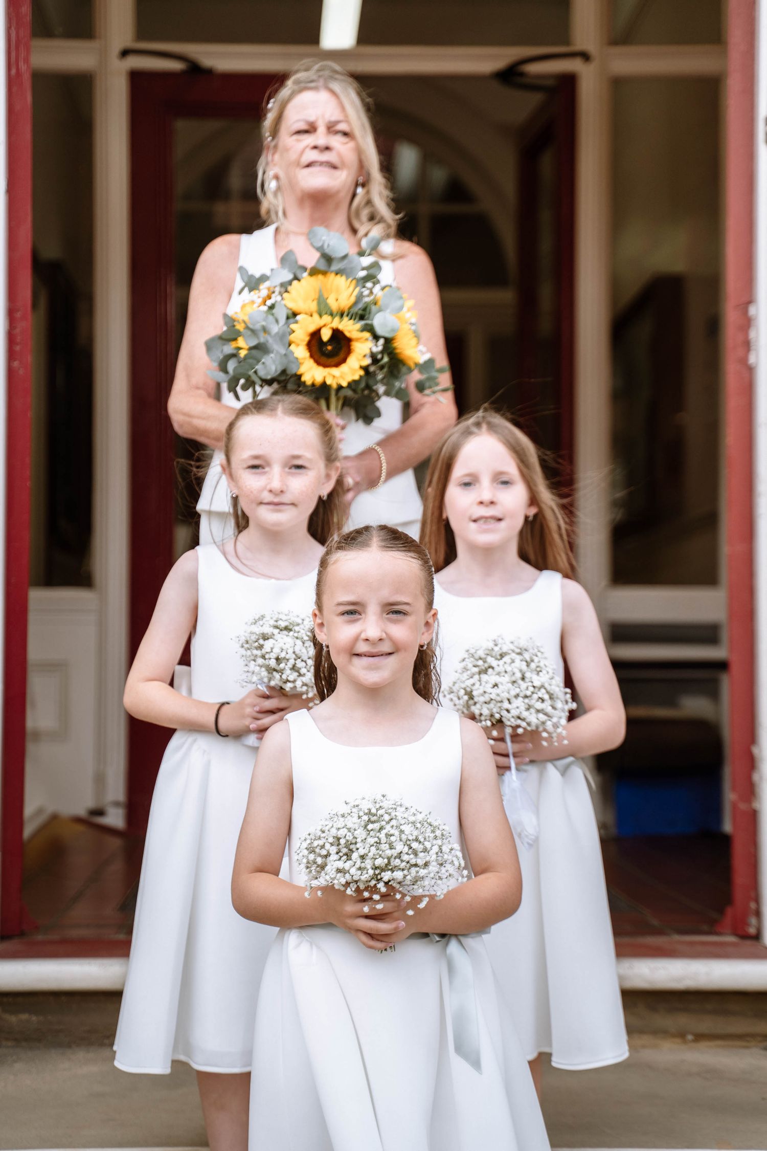 Bride holding a sunflower bouquet standing behind three flower girls in white dresses outside Waterloo Town Hall