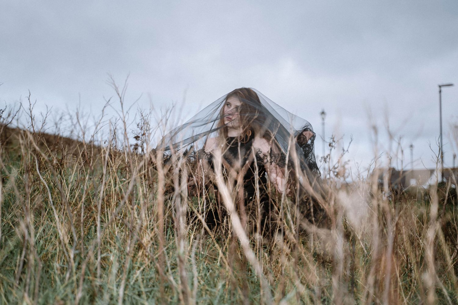 Person in black dress with veil in grass during Cornwall Elopement in St Ives