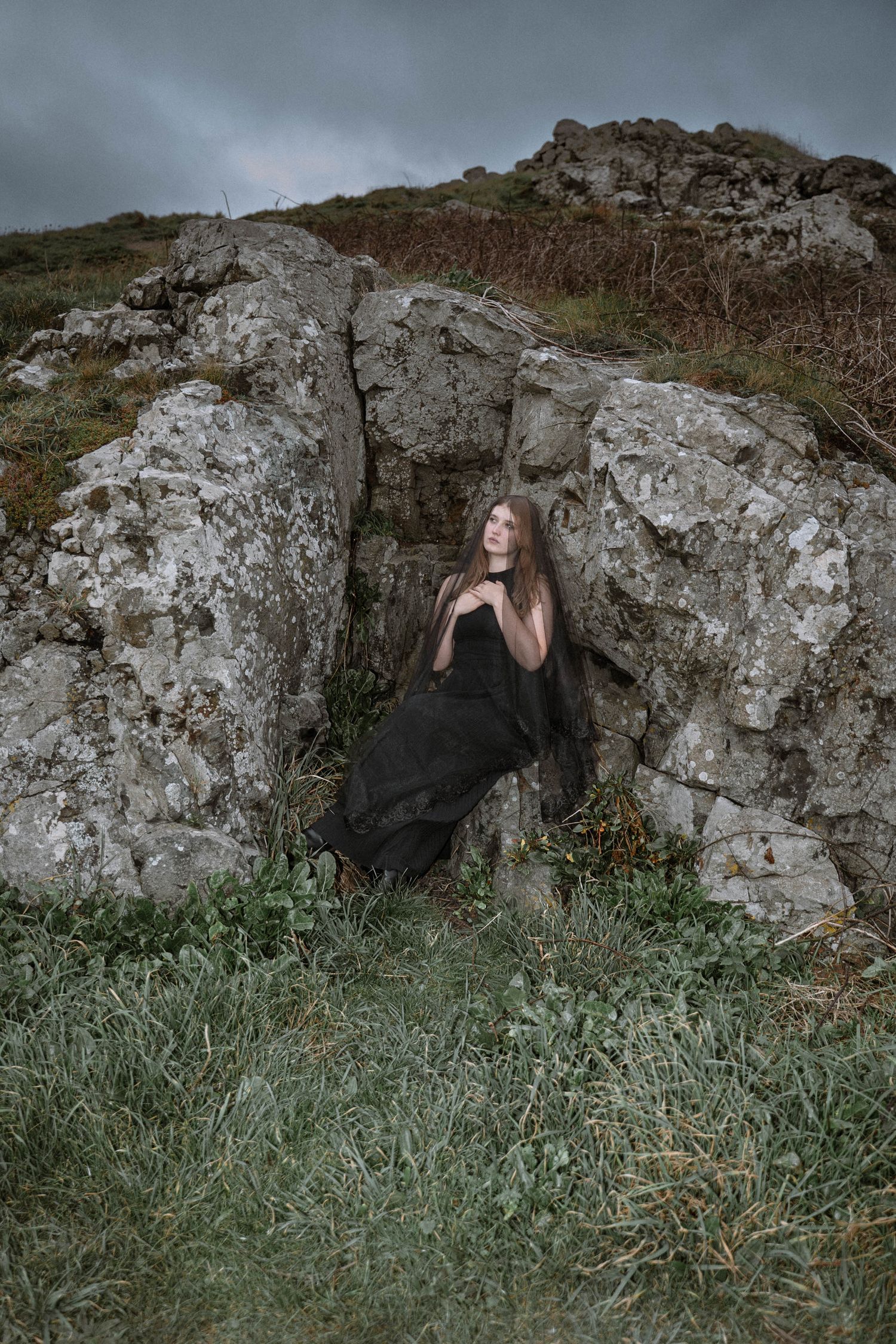 Cornwall gothic wedding portrait bride in black dress standing against rocky cliff moody coastal elopement photography UK