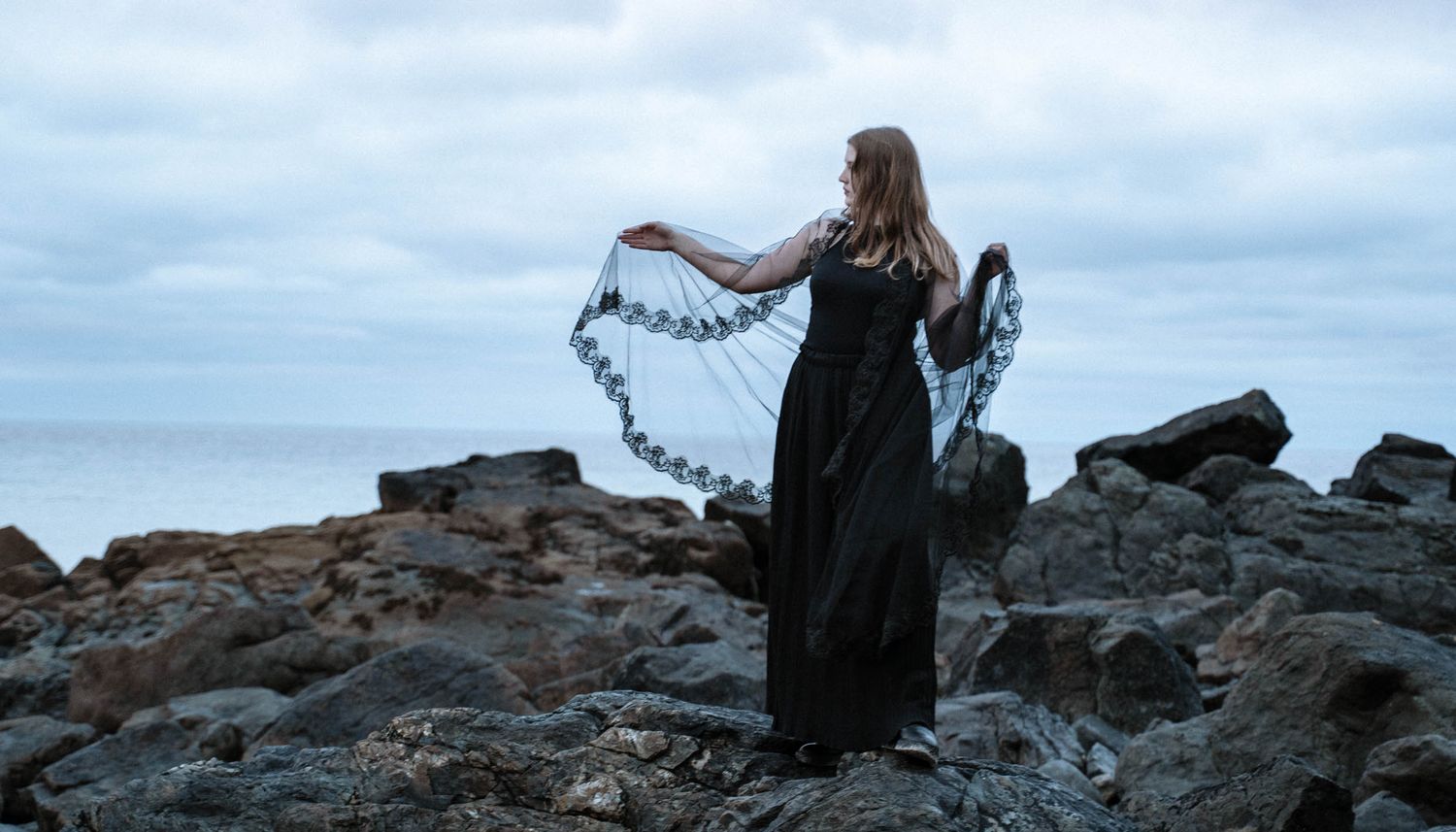 Cornwall gothic wedding coastal portrait bride holding veil on rocks dramatic seaside elopement photography Cornwall