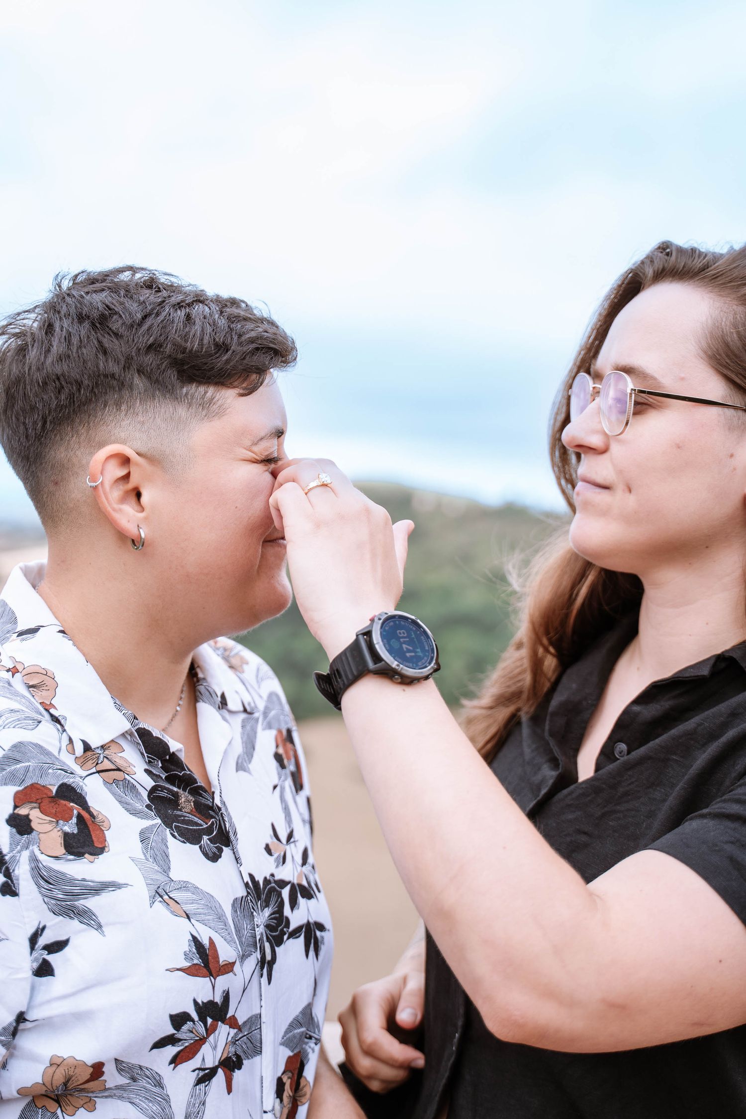 A queer couple face each other as one gently touches the other’s face.