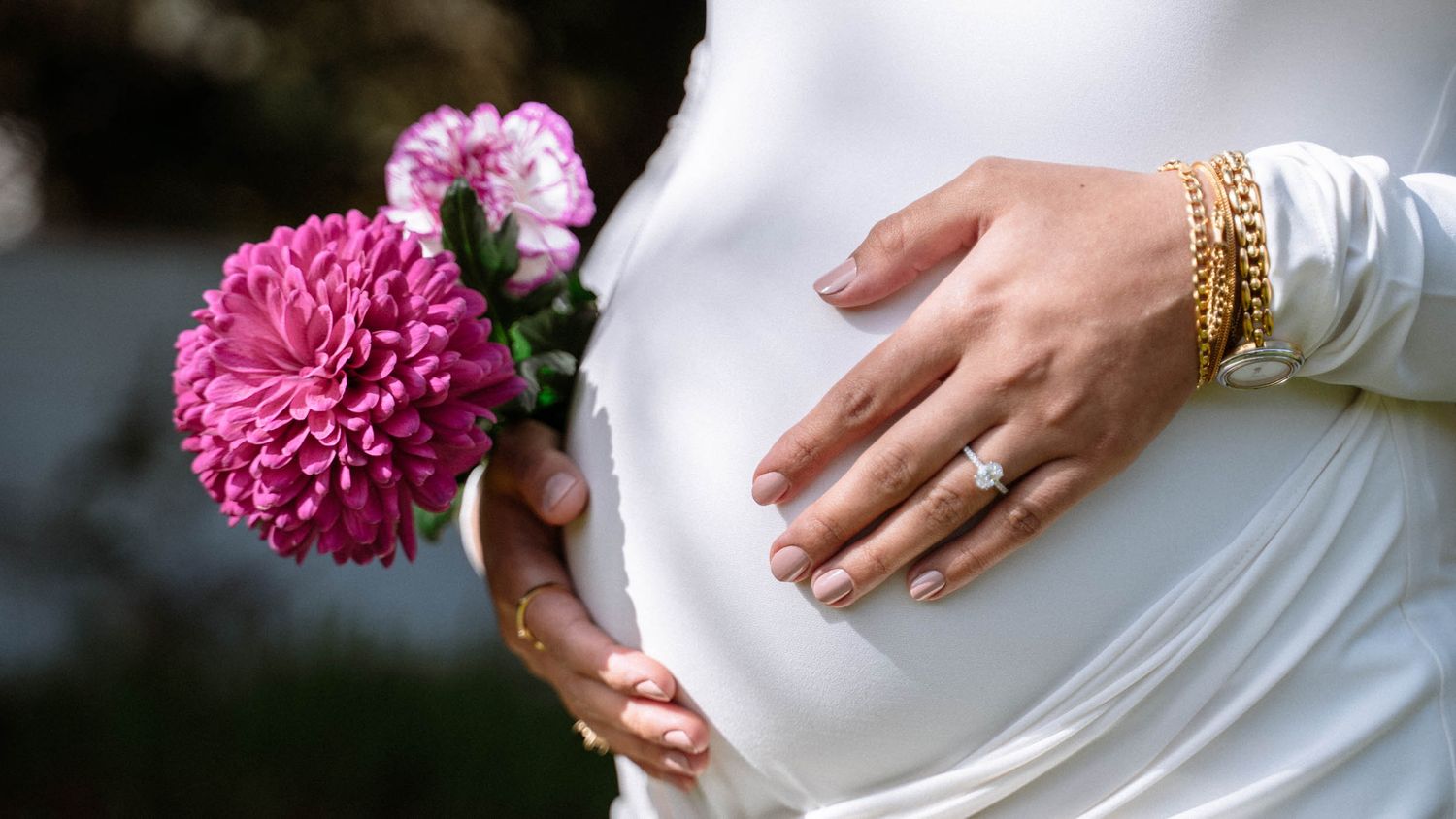 Close-up of a pregnant woman’s hands and pink flowers against her white dress