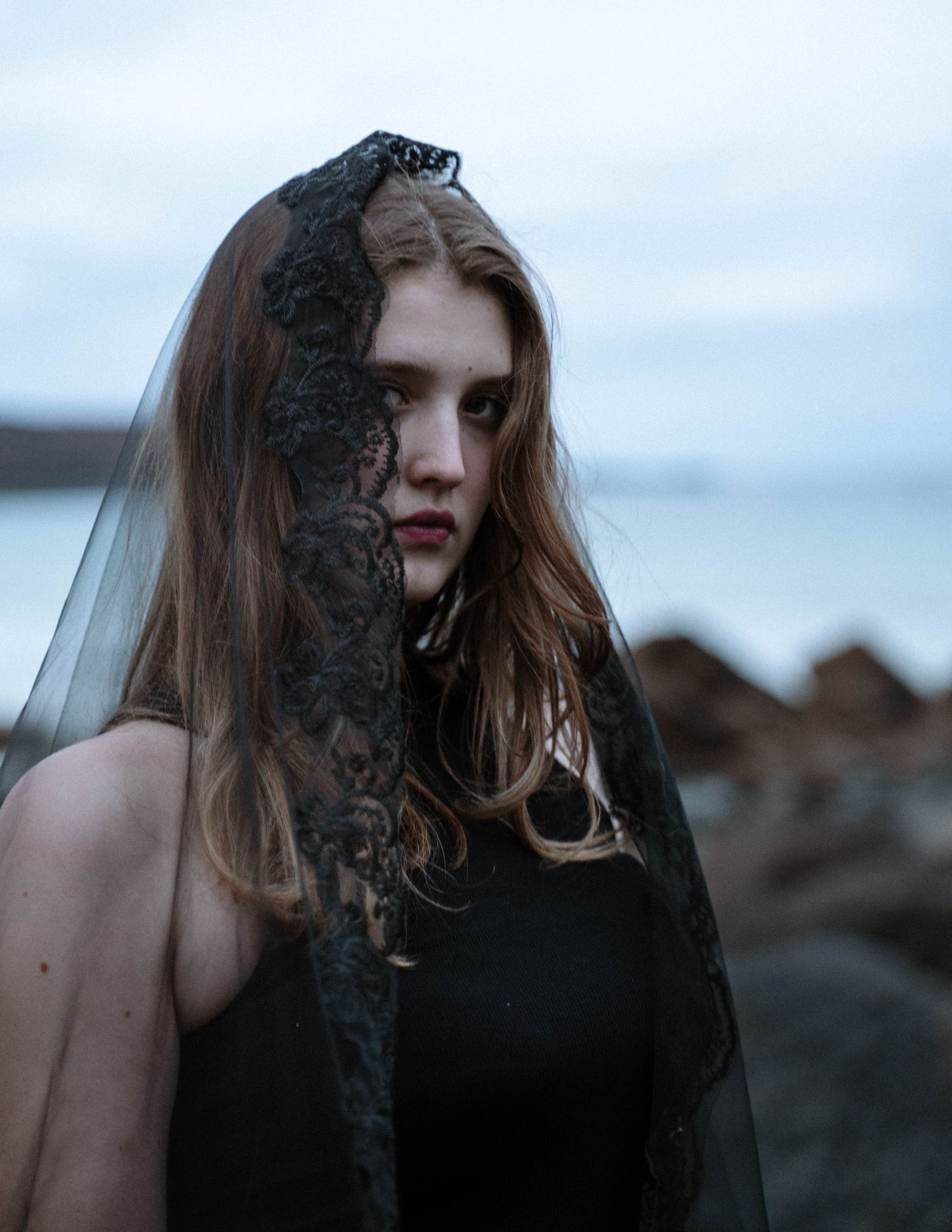 Close up portrait of bride in black dress on Cornwall coastline with moody sky