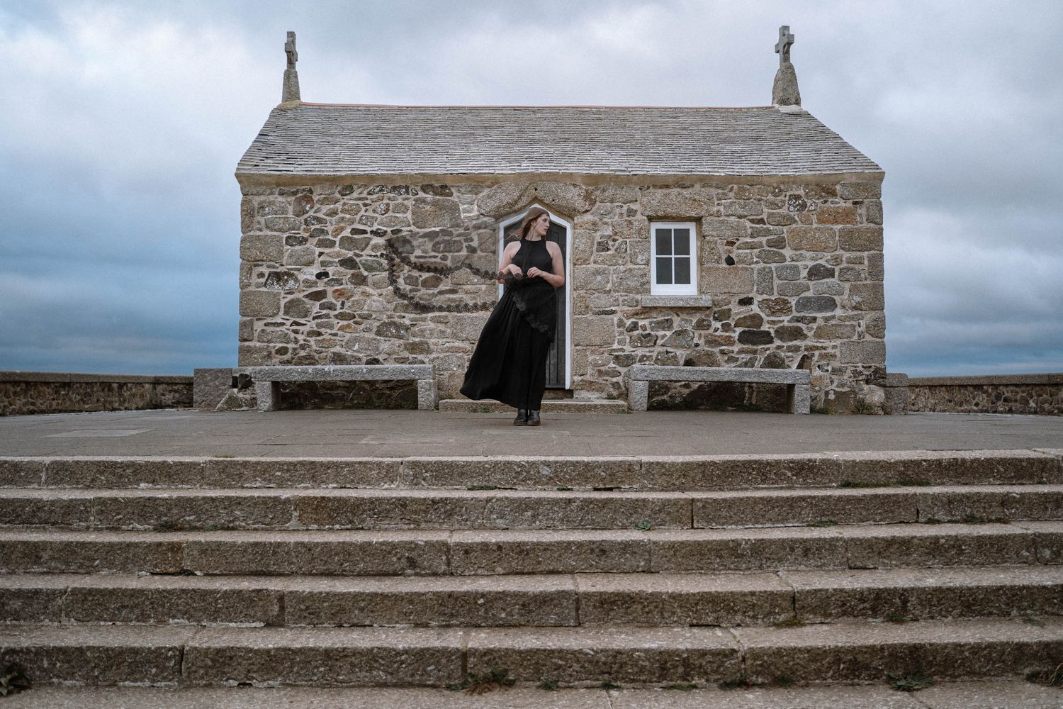 Person in black dress standing outside stone chapel during a St Ives Cornwall elopement with gothic editorial styling