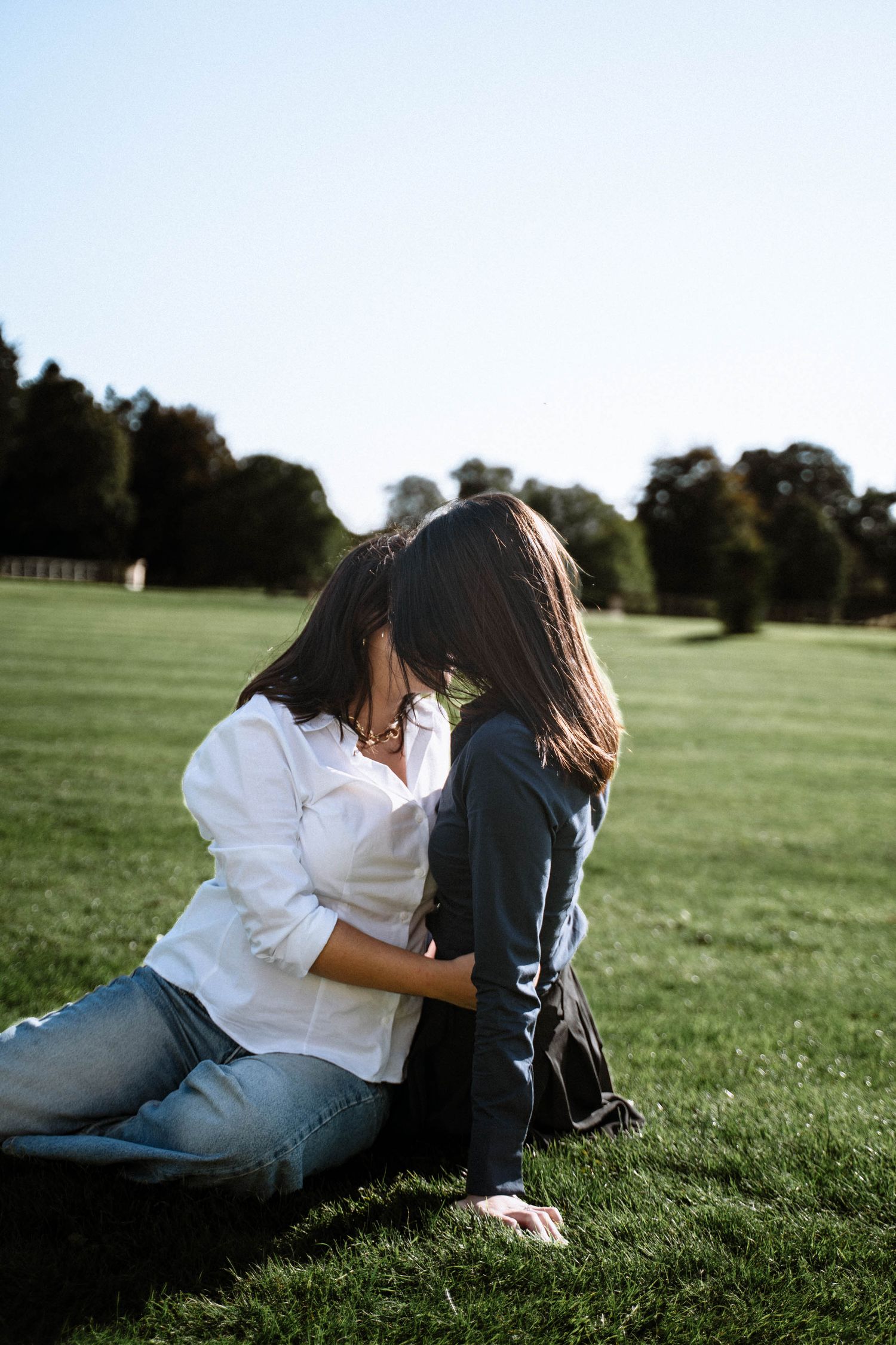 Cardiff proposal photoshoot couple sitting on grass embracing in open field during natural engagement session in Wales