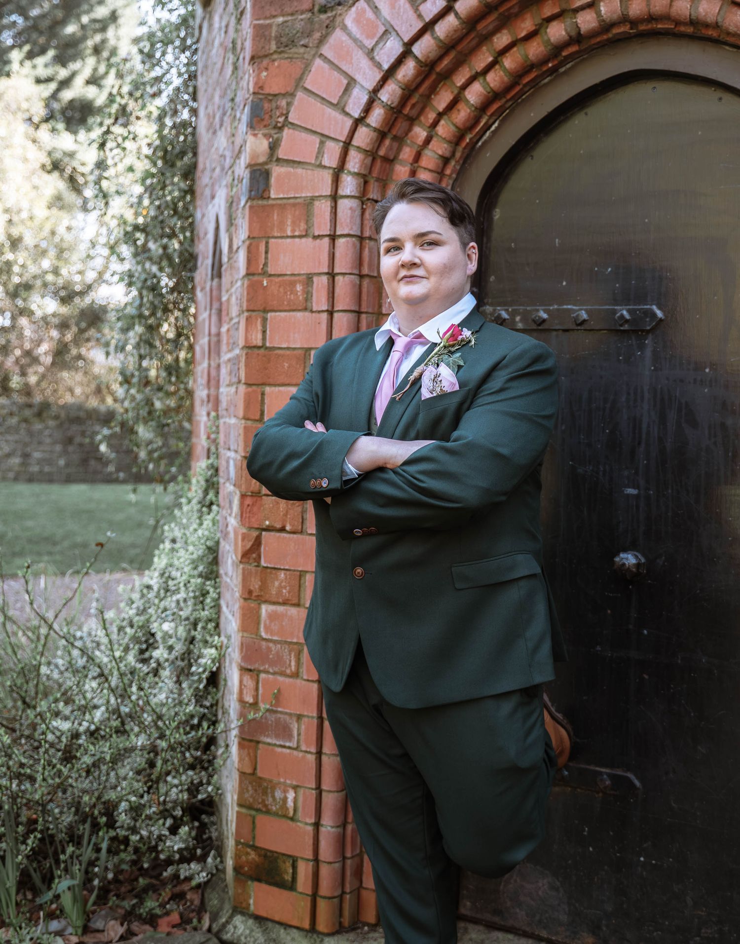 Bride standing confidently in suit outside brick arch doorway in Manchester