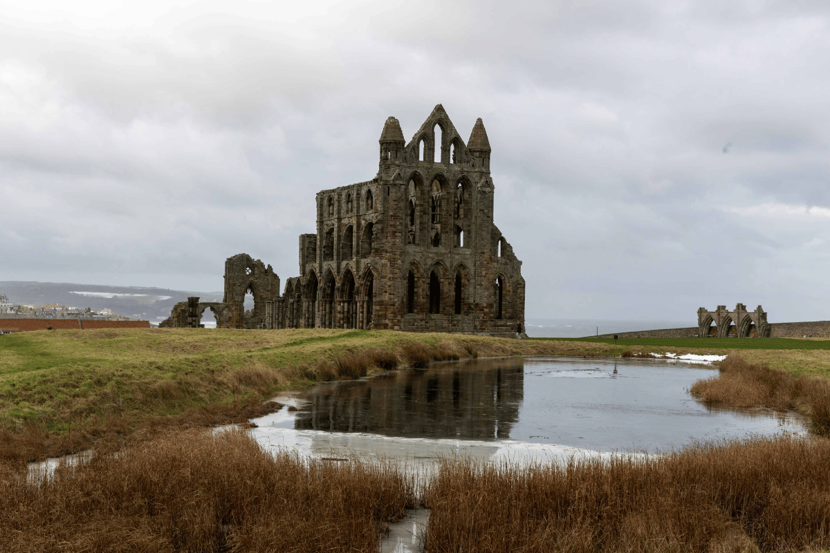 Whitby Abbey ruins stand dramatically against a cloudy sky on the Yorkshire coast in England.