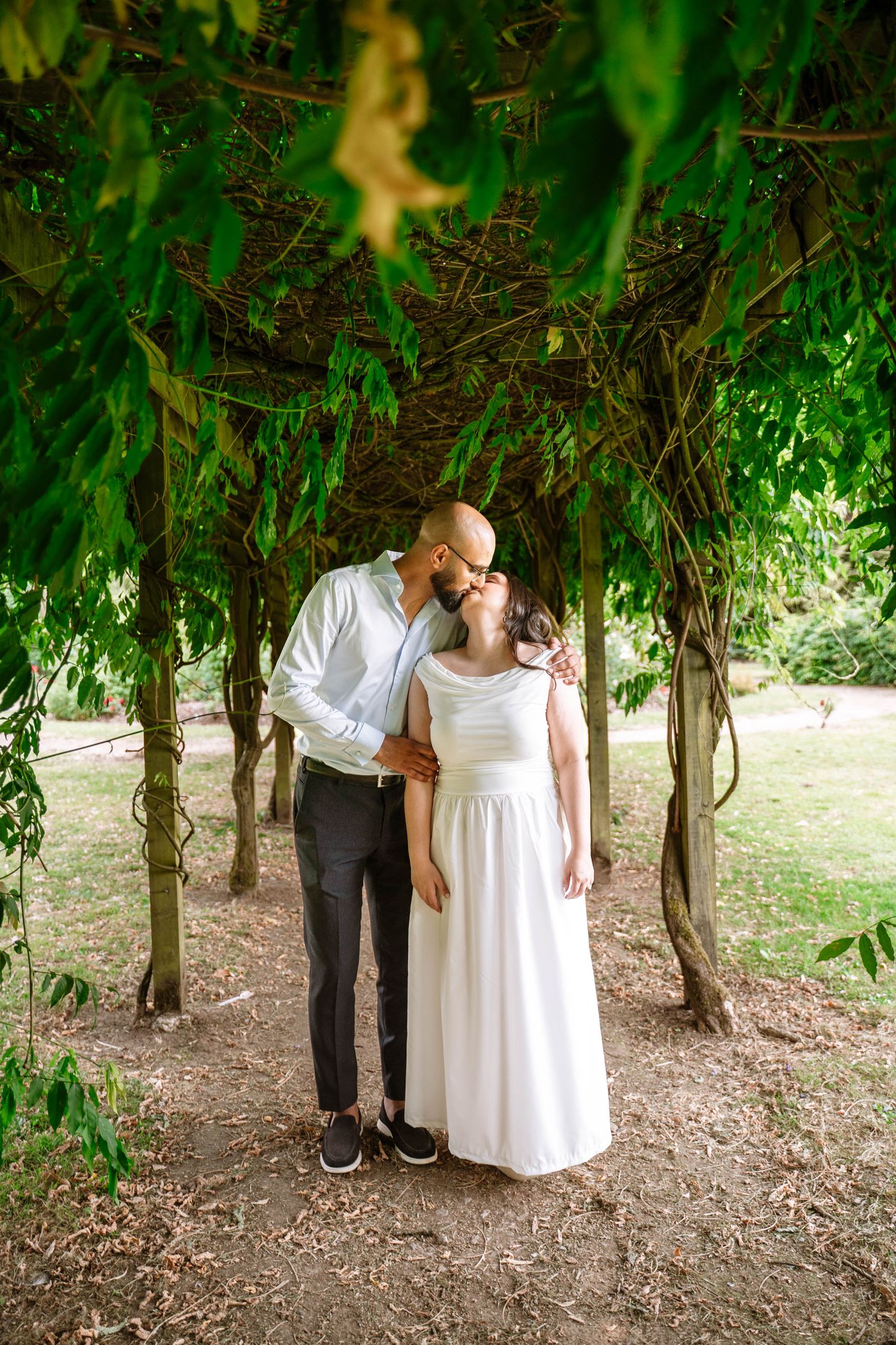 Couple kissing beneath the a foilage arch during a Fletcher Moss Park proposal