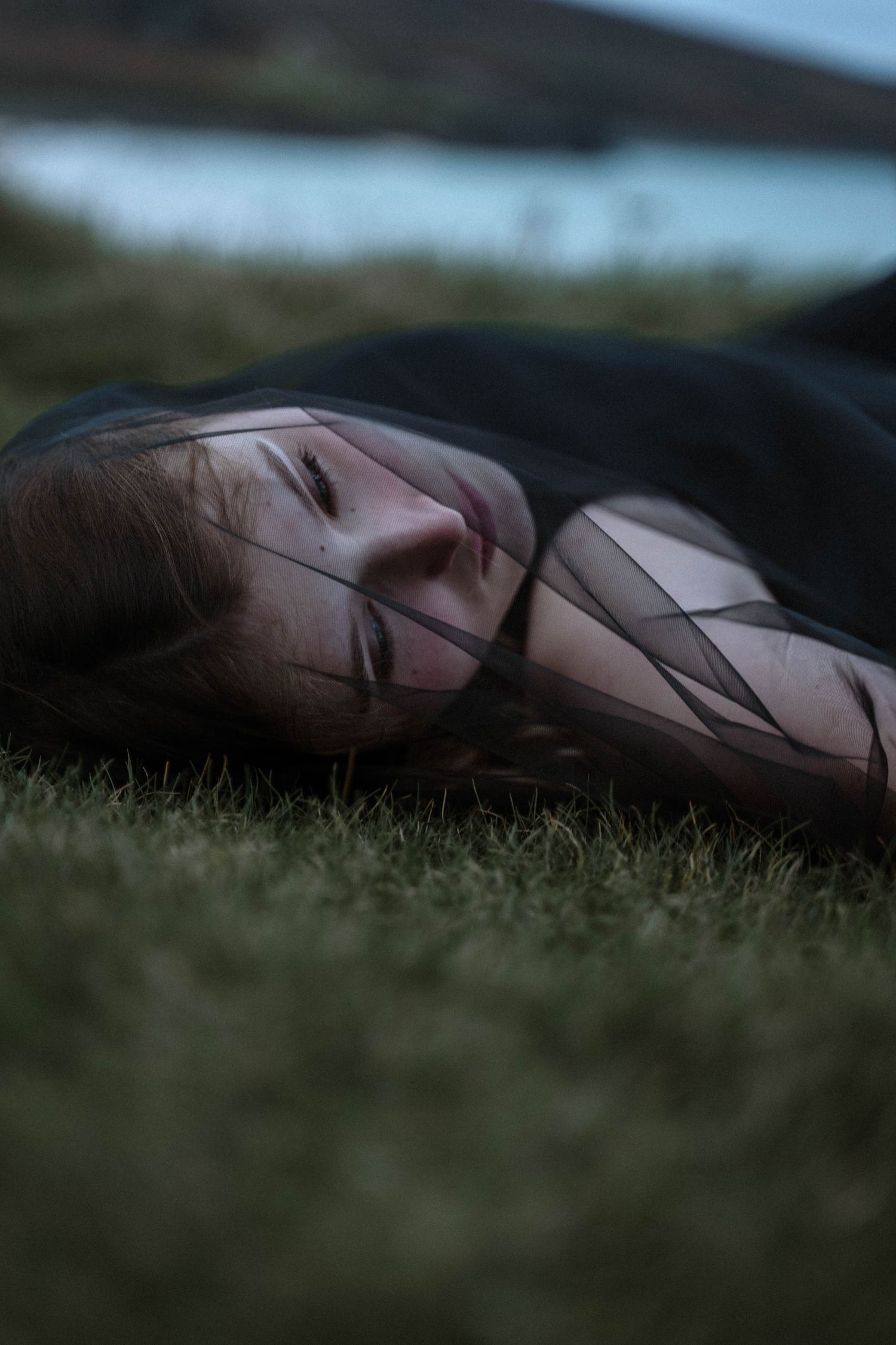 Woman lying on grass in Cornwall during a gothic styled bridal shoot at blue hour