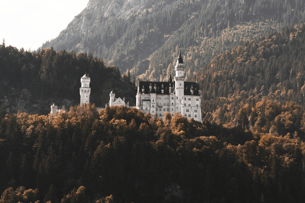 Neuschwanstein Castle rises majestically from autumn forest in Bavaria with its white towers against mountain backdrop.