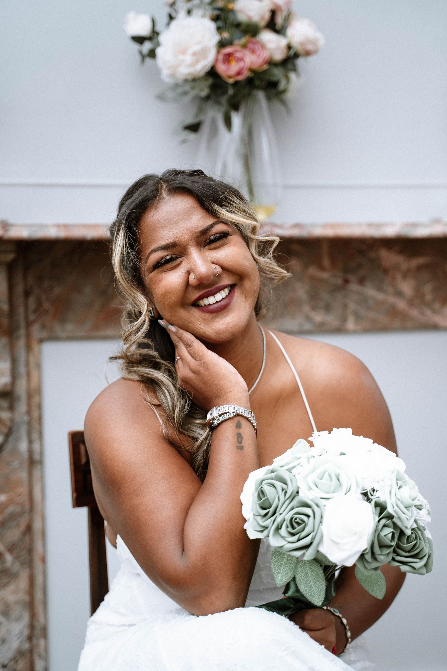 Bride in white halter dress smiles joyfully while holding a bouquet of sage green and white roses.