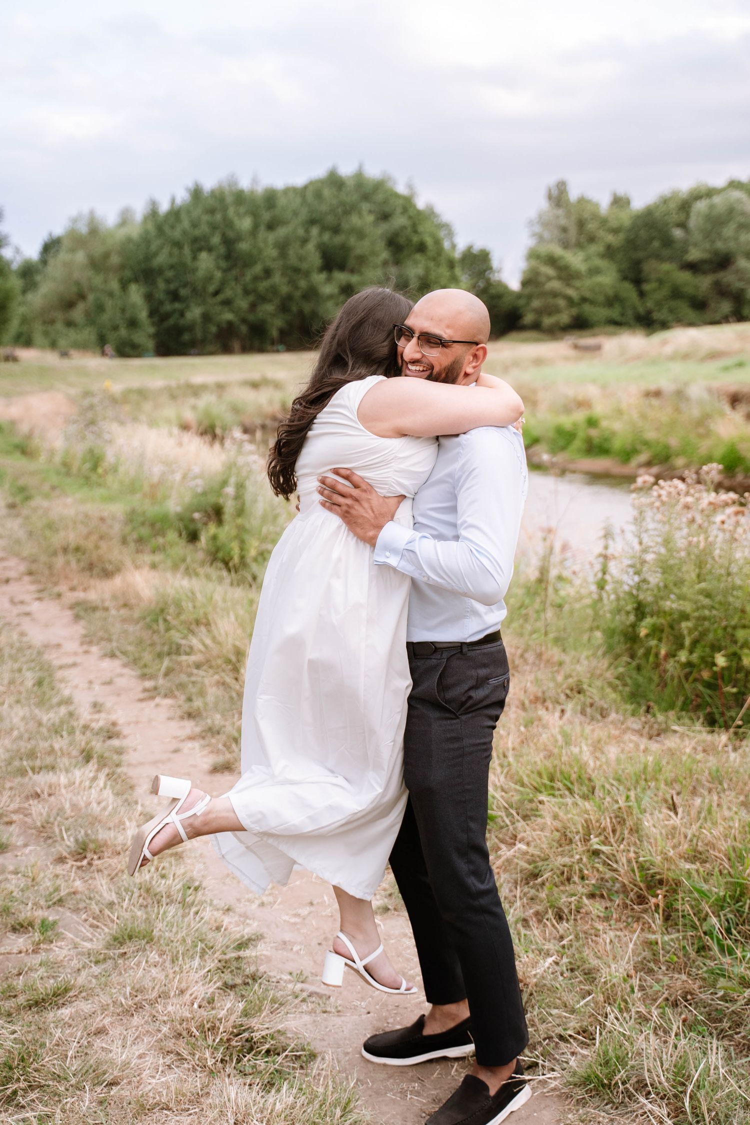 Couple embracing in an open meadow during their Fletcher Moss Park proposal