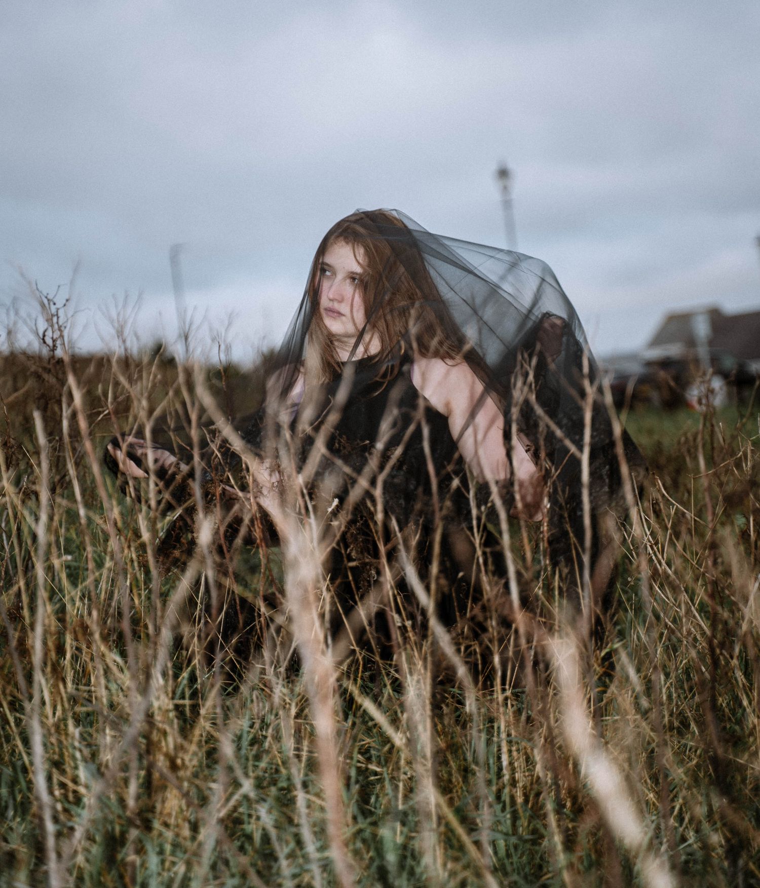 Artistic portrait in tall grass on St Ives cliffs during a Cornwall elopement with lighthouse in the background under an overcast sky