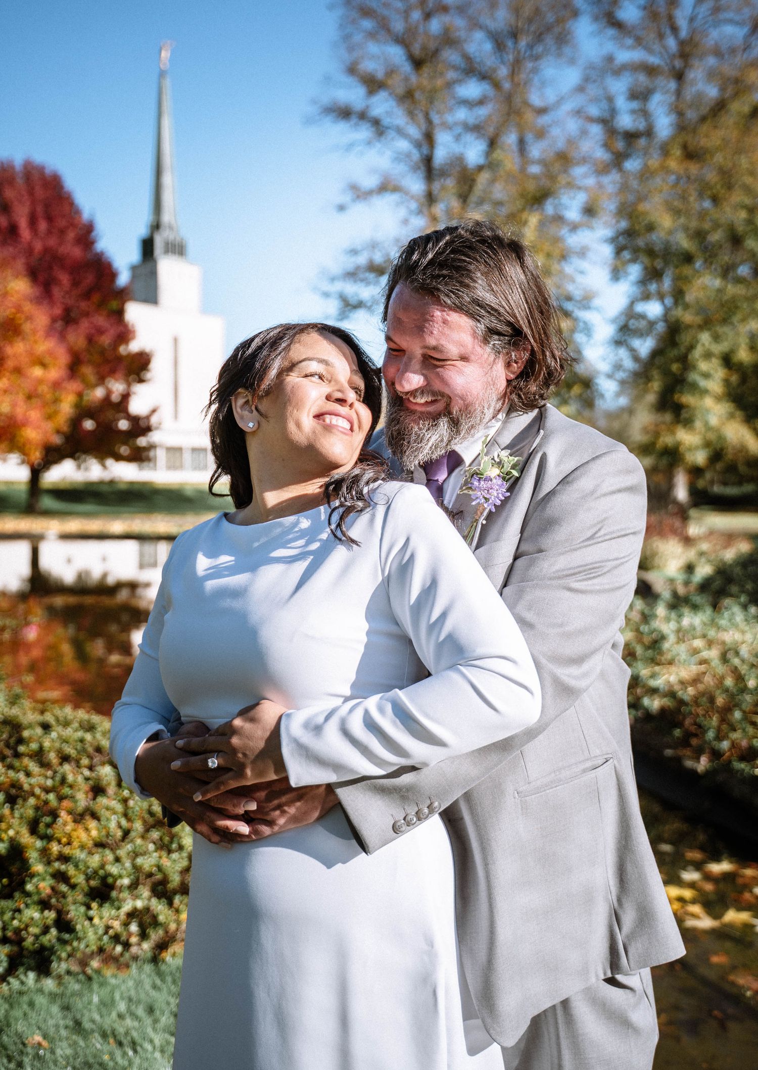 Couple embracing outdoors near LDS temple during autumn wedding portraits