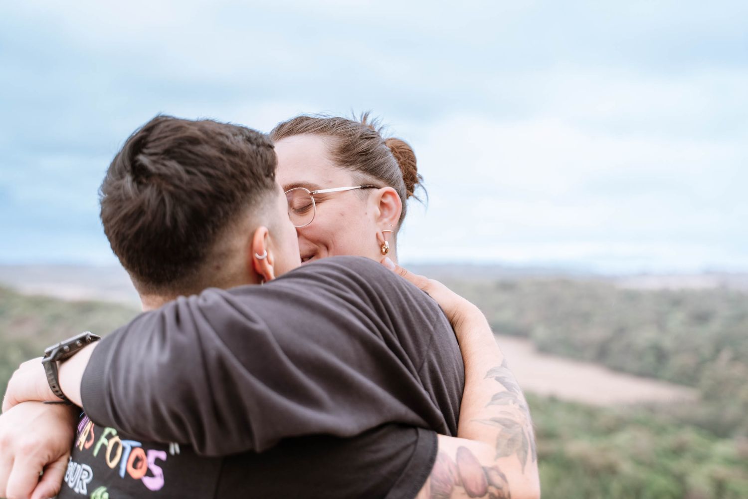 A lesbian couple kiss while embracing above the Wye Valley at Symonds Yat Rock.