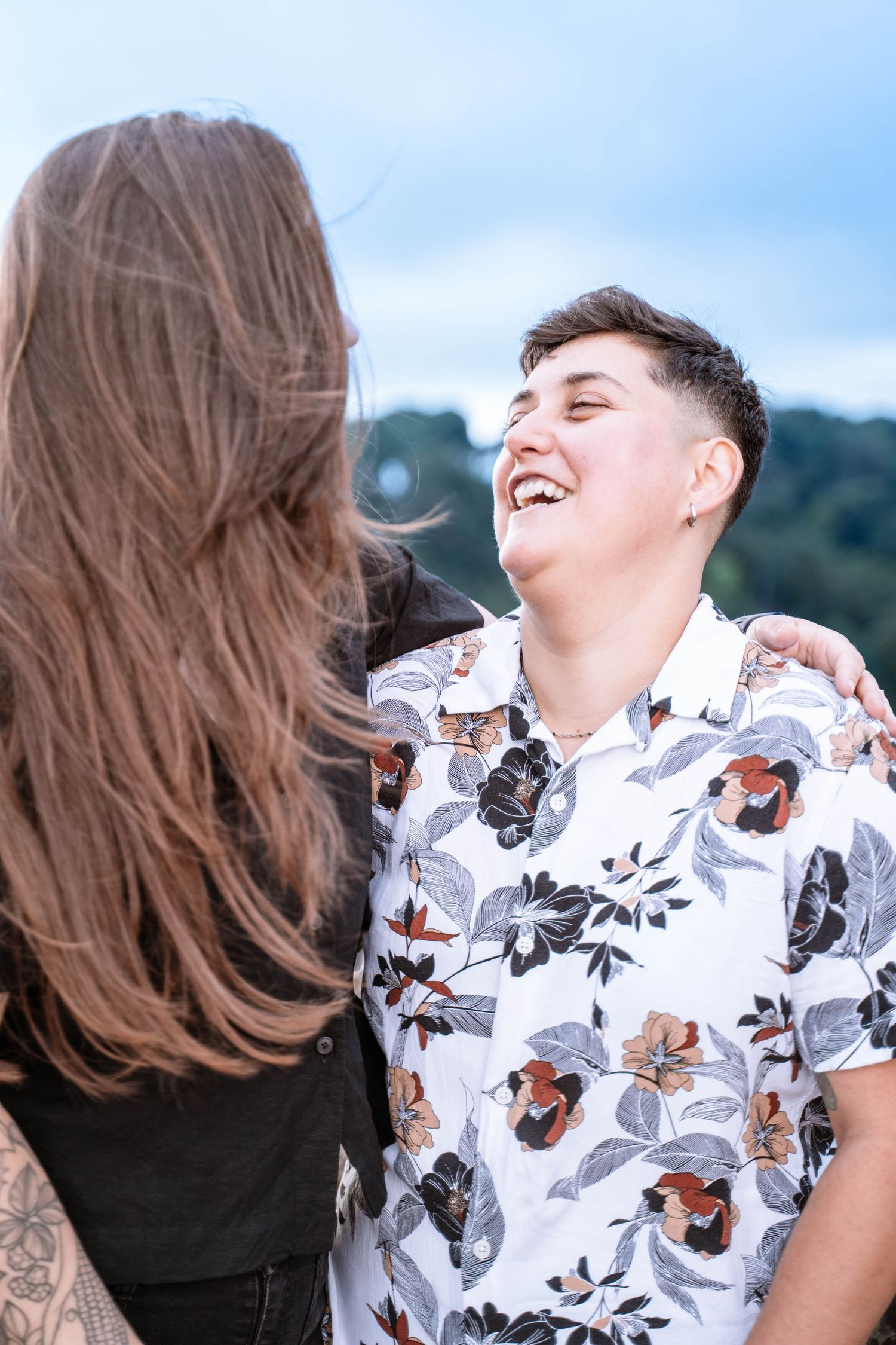 A lesbian couple laughing together during proposal portraits at Symonds Yat Rock.